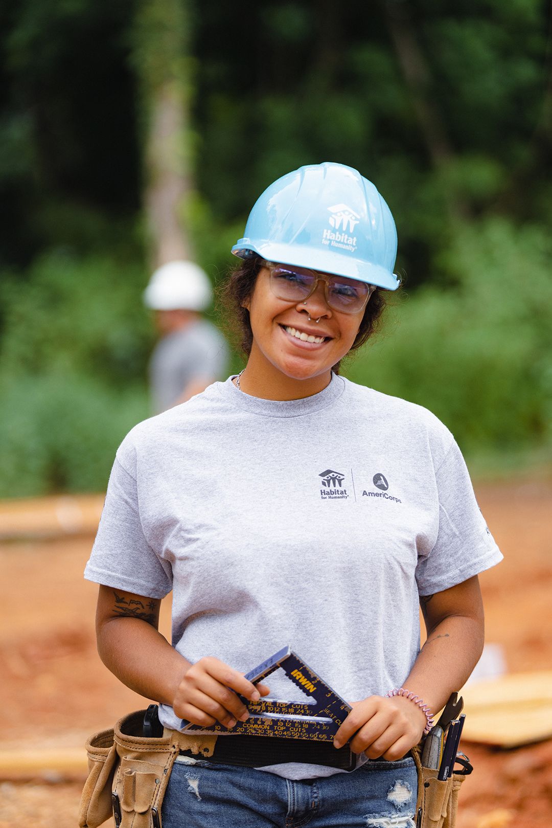 A young woman AmeriCorps volunteer smiles while working to raise walls on a build site.