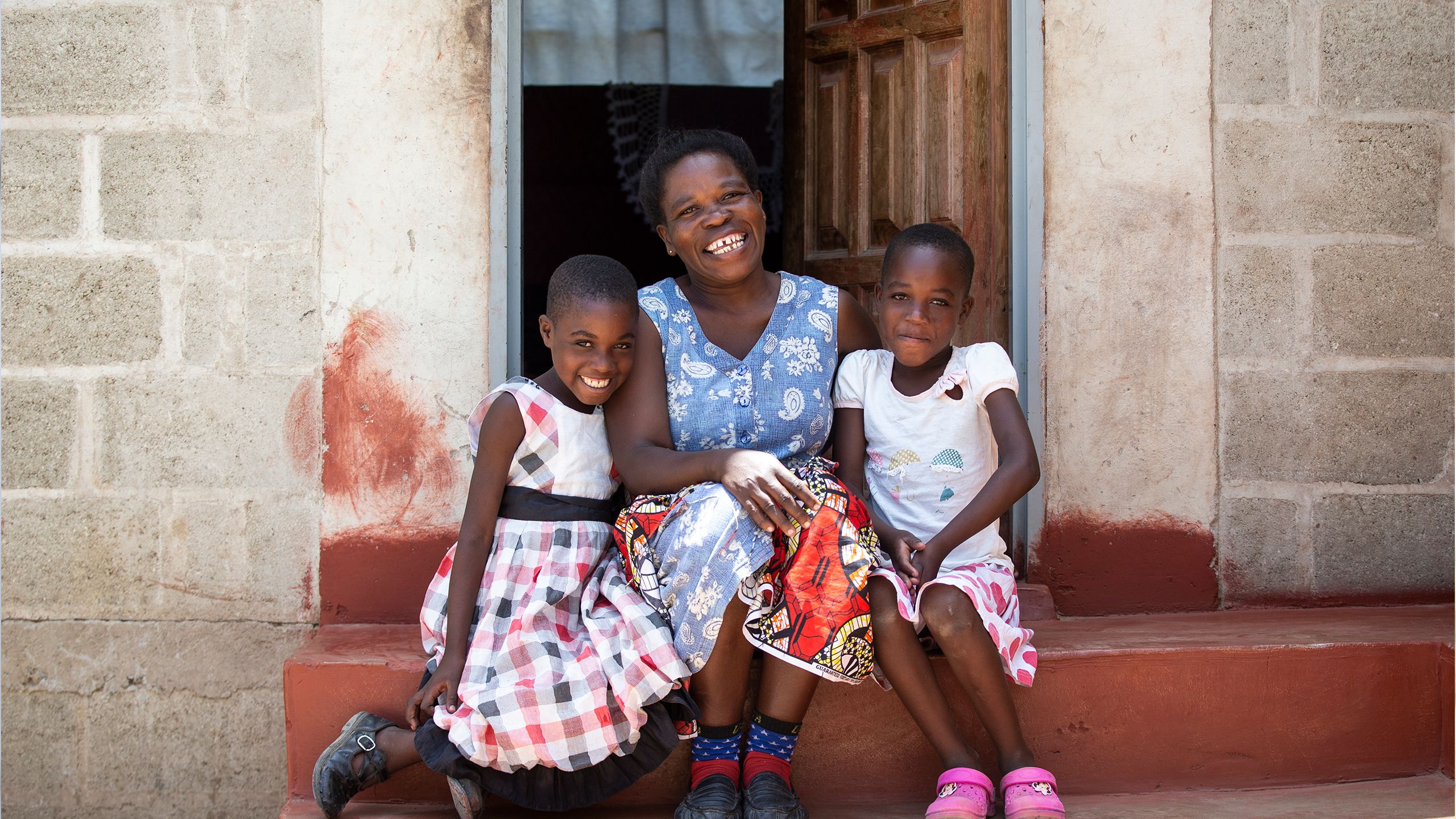A mother and her two daughters sit on the stoop of their Habitat home in Zambia.