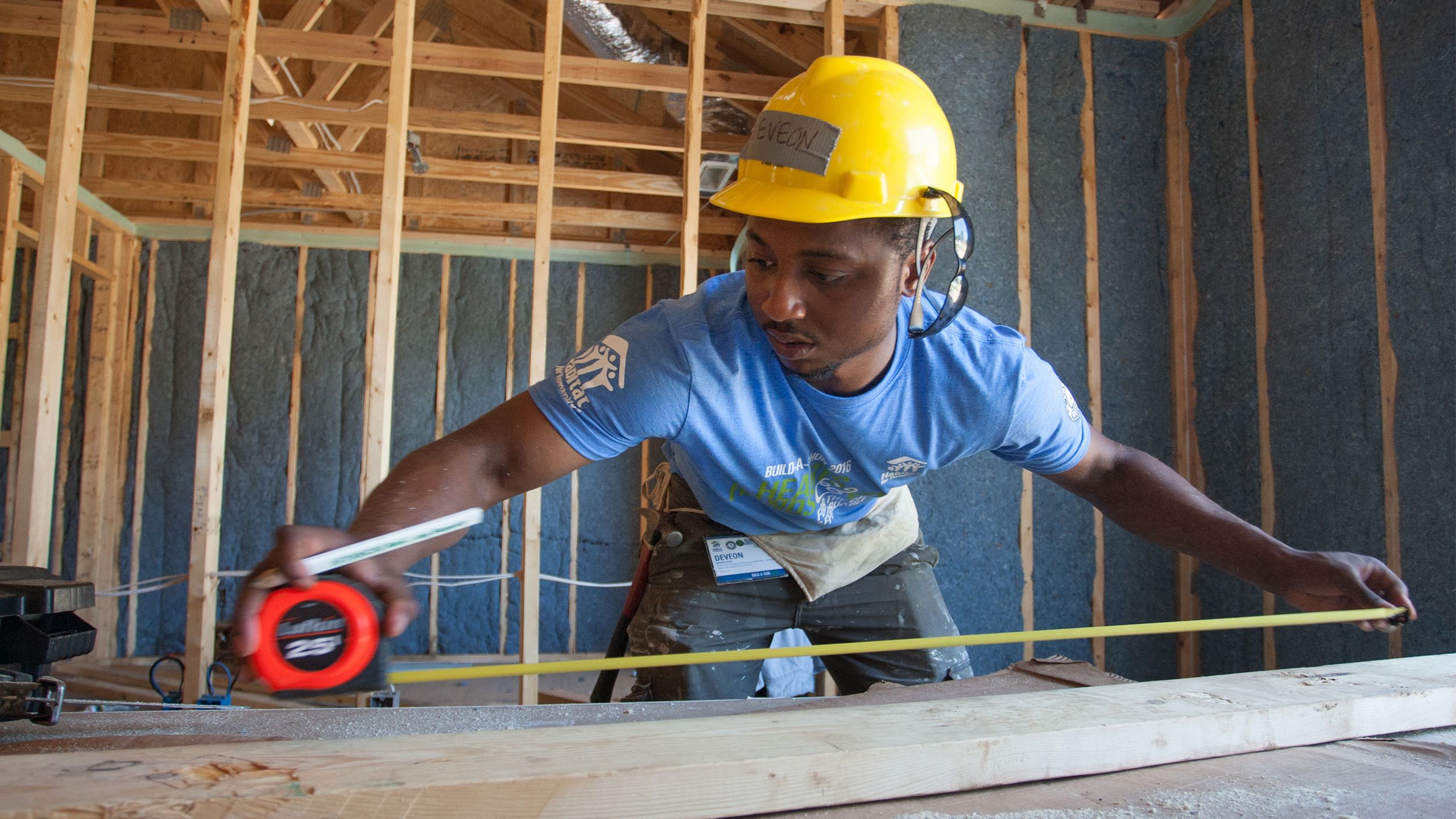 An AmeriCorps member concentrates as he measures a piece of lumber with a measuring tape.