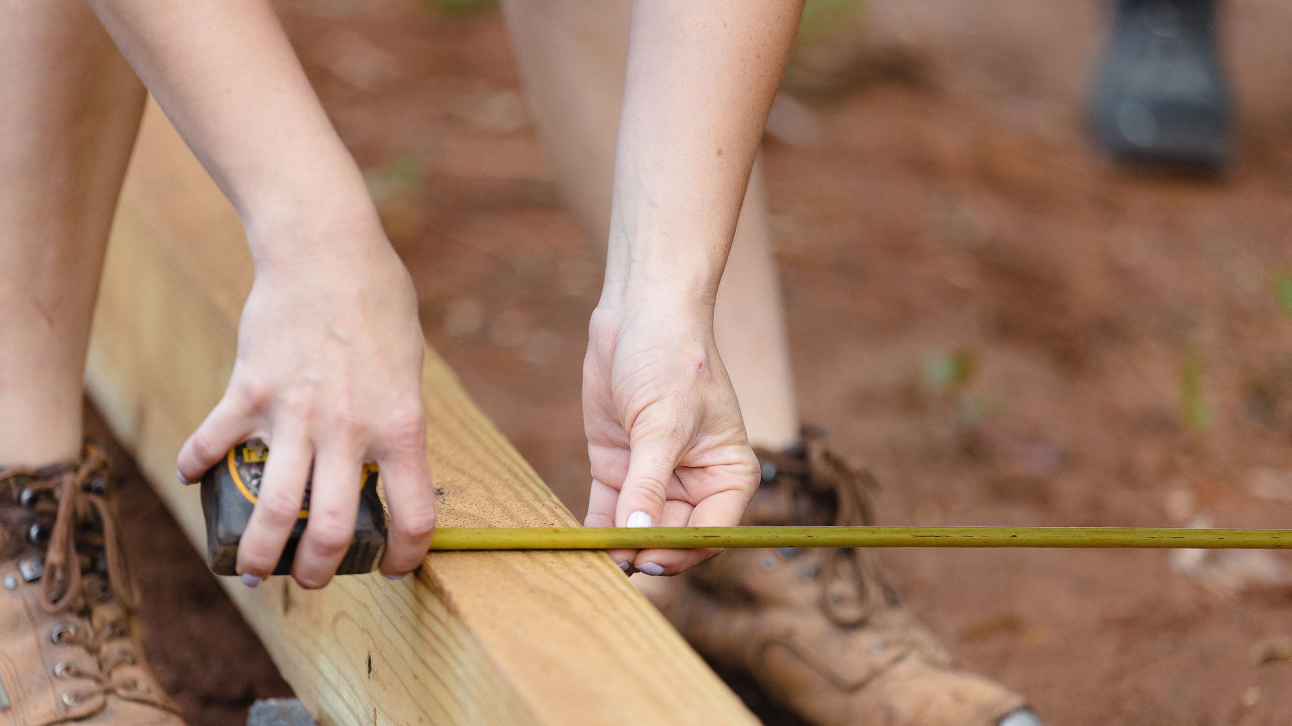 A volunteer measures and marks a wood plank.