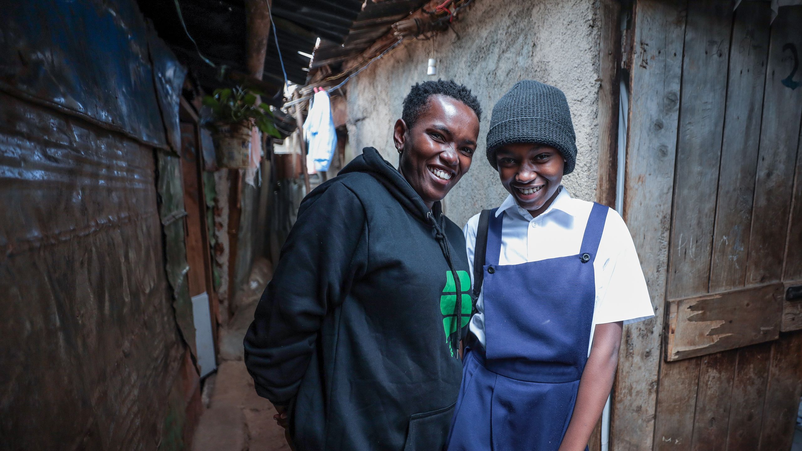 Milka and her daughter, who is wearing a school uniform, pose for a portrait at the door of their home in Kibera.