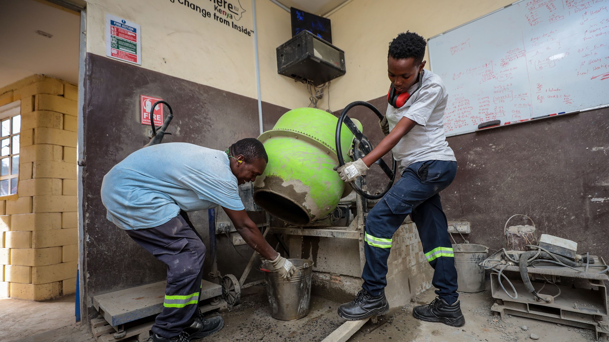 In the Start Somewhere workshop, Milka tilts a concrete mixer to fill the bucket her coworker is holding.