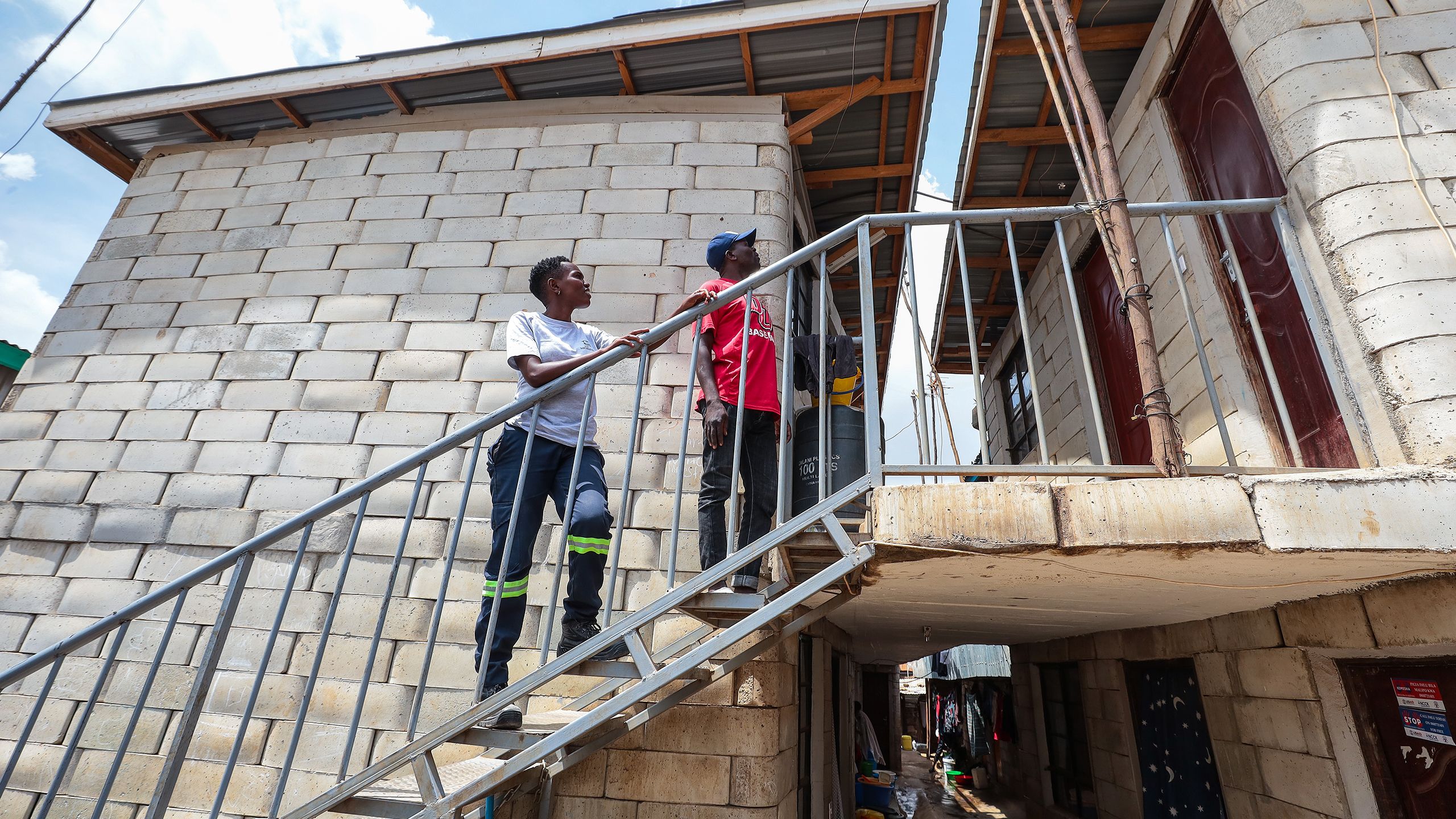 Milka and another builder stand on the staircase of a completed two-story building made with TwistBlocks.