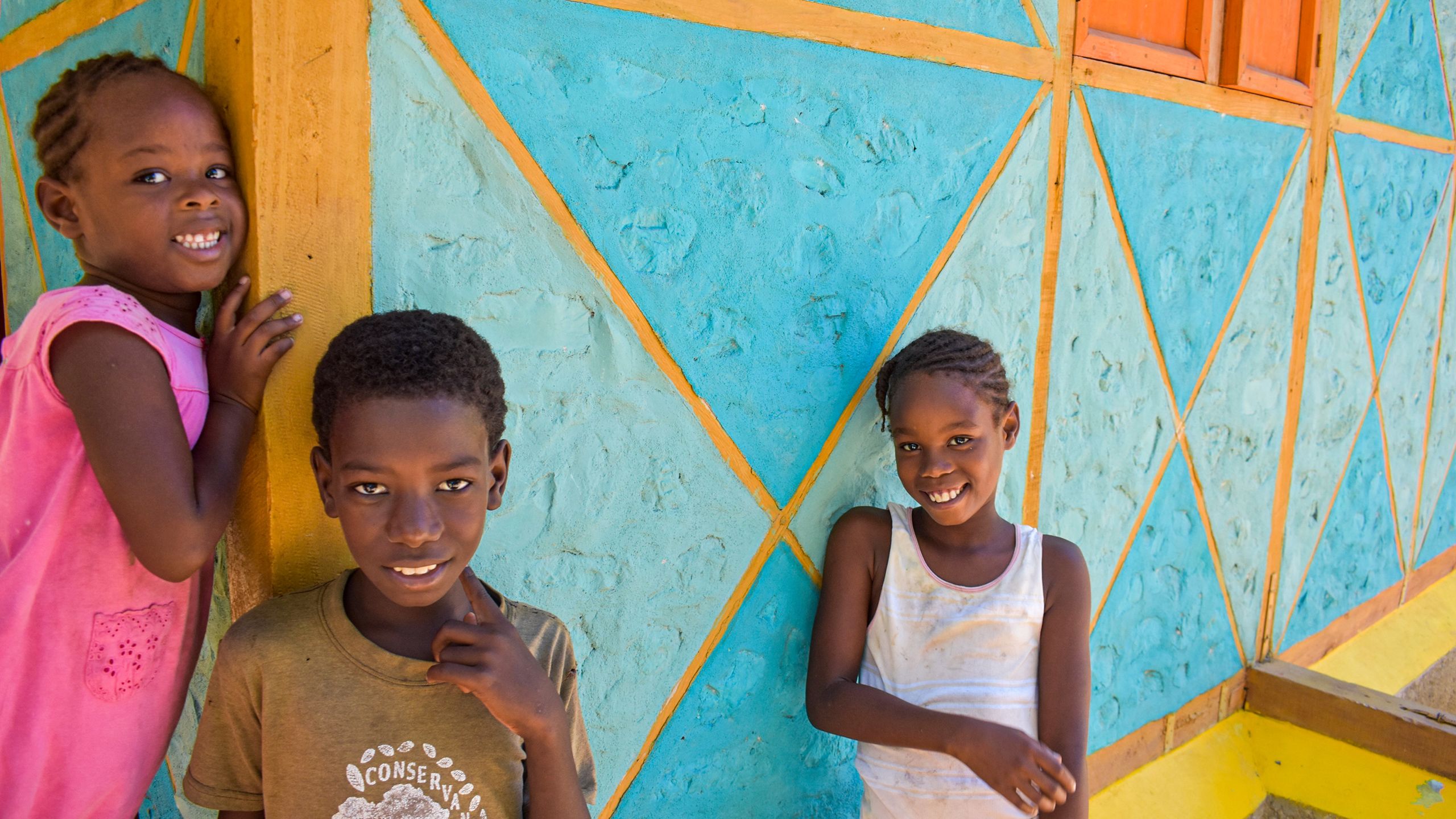 tres niños haitianos fuera de su nueva vivienda Hábitat.