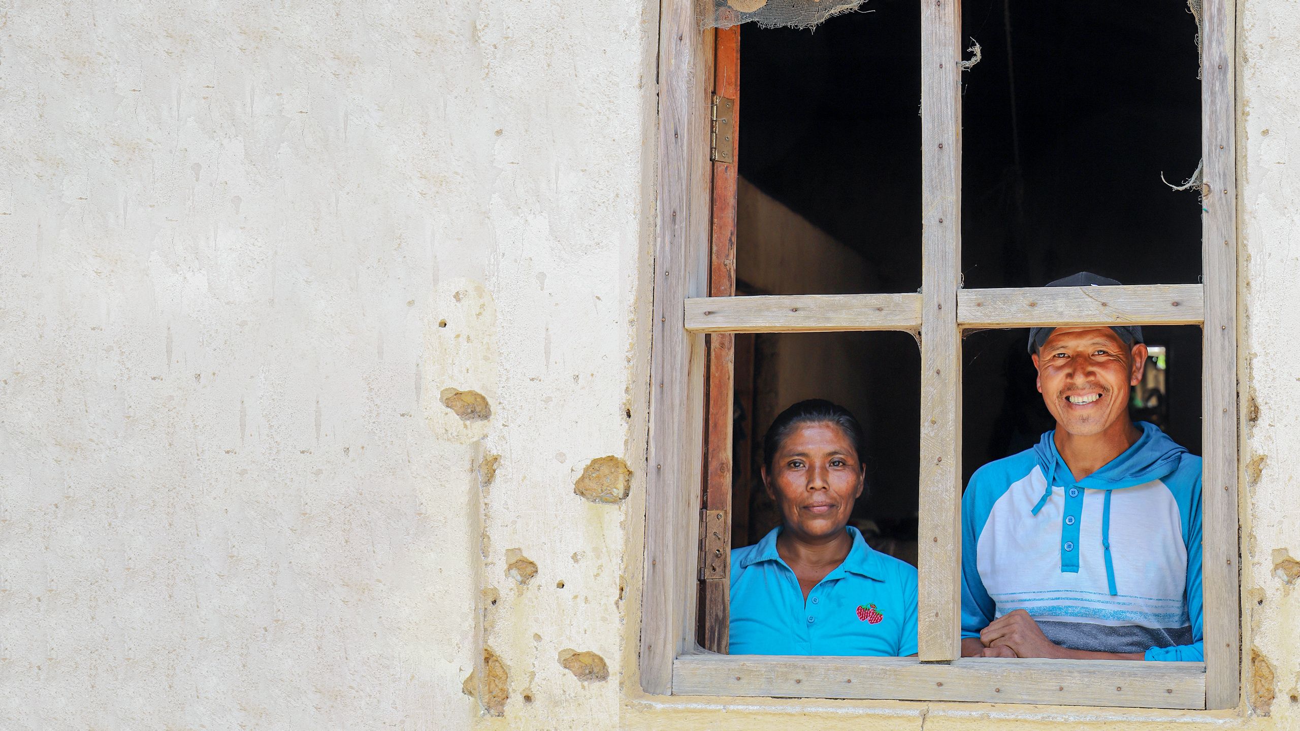 hombre y mujer sonriendo tras una ventana de madera.