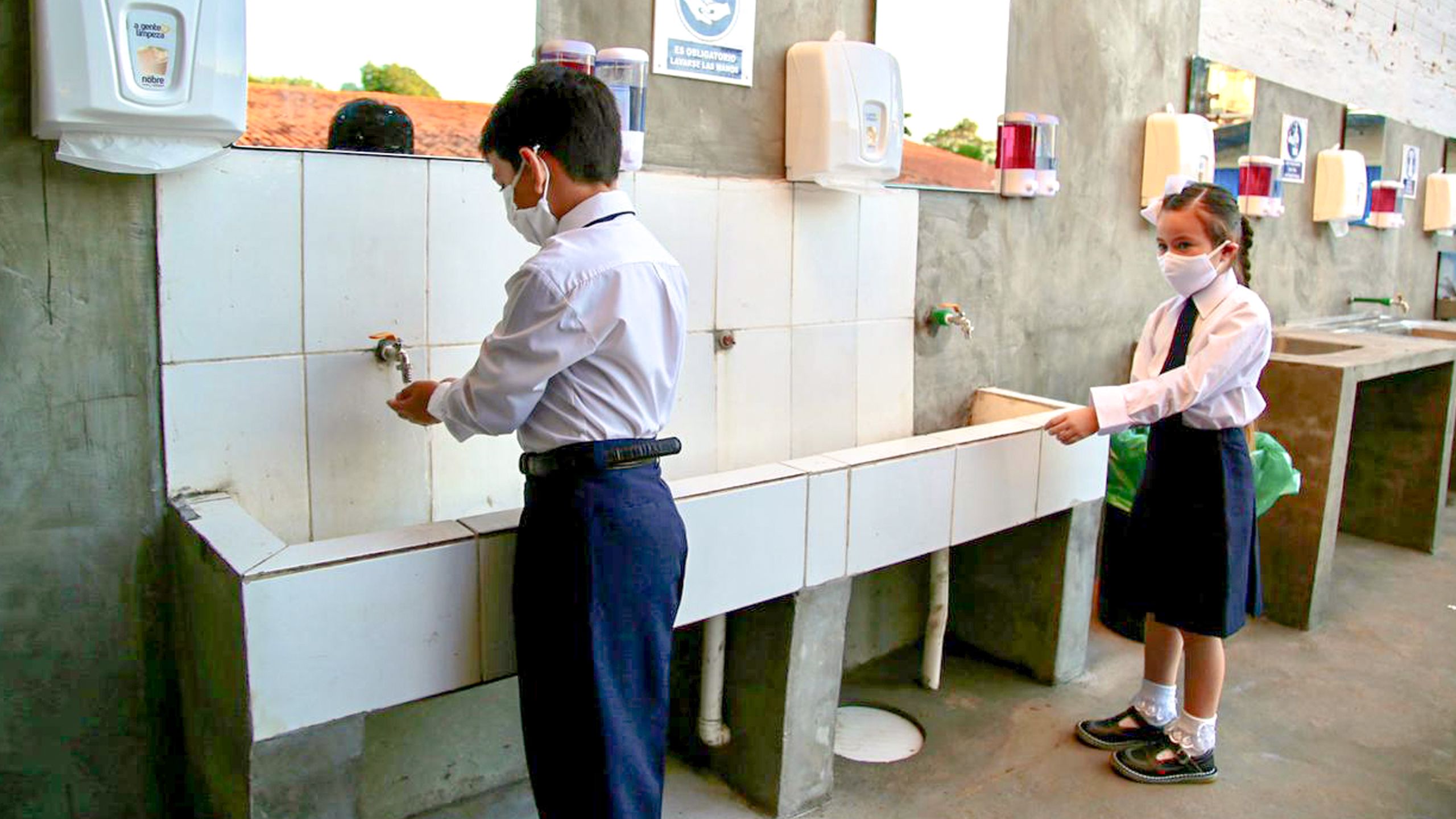 Boy and girl in school uniform washing their hands.