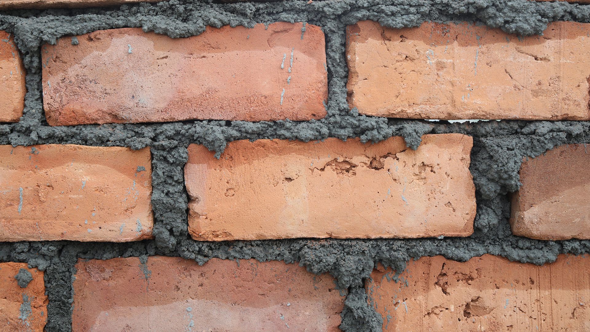 Closeup of a red clay brick wall with drying mortar.