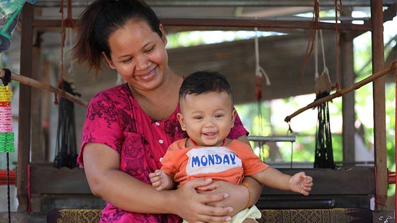 Cambodian homeowner Senghouch with her child in front of her weaving loom