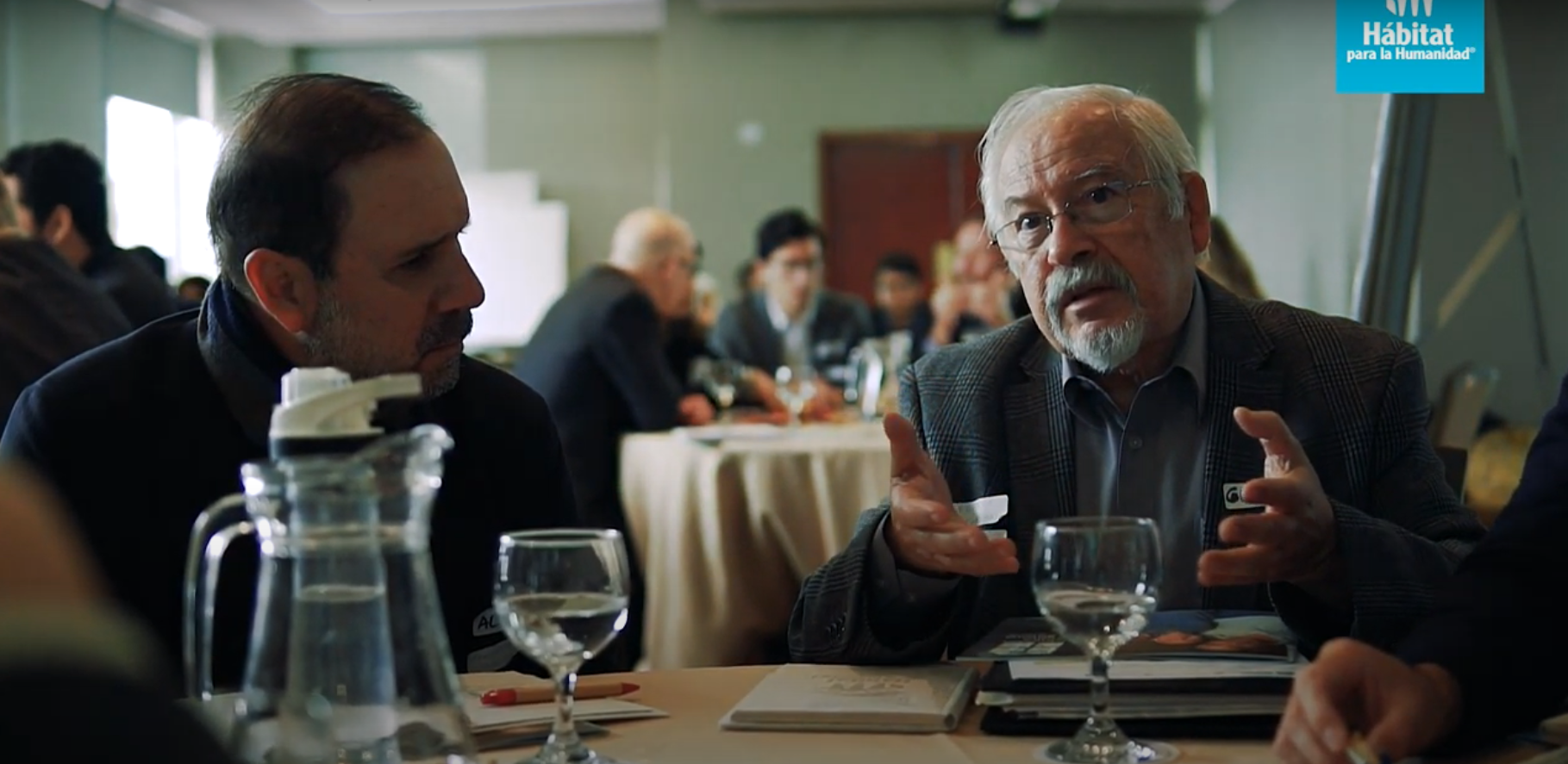 A man talks to a group while sitting at a table.
