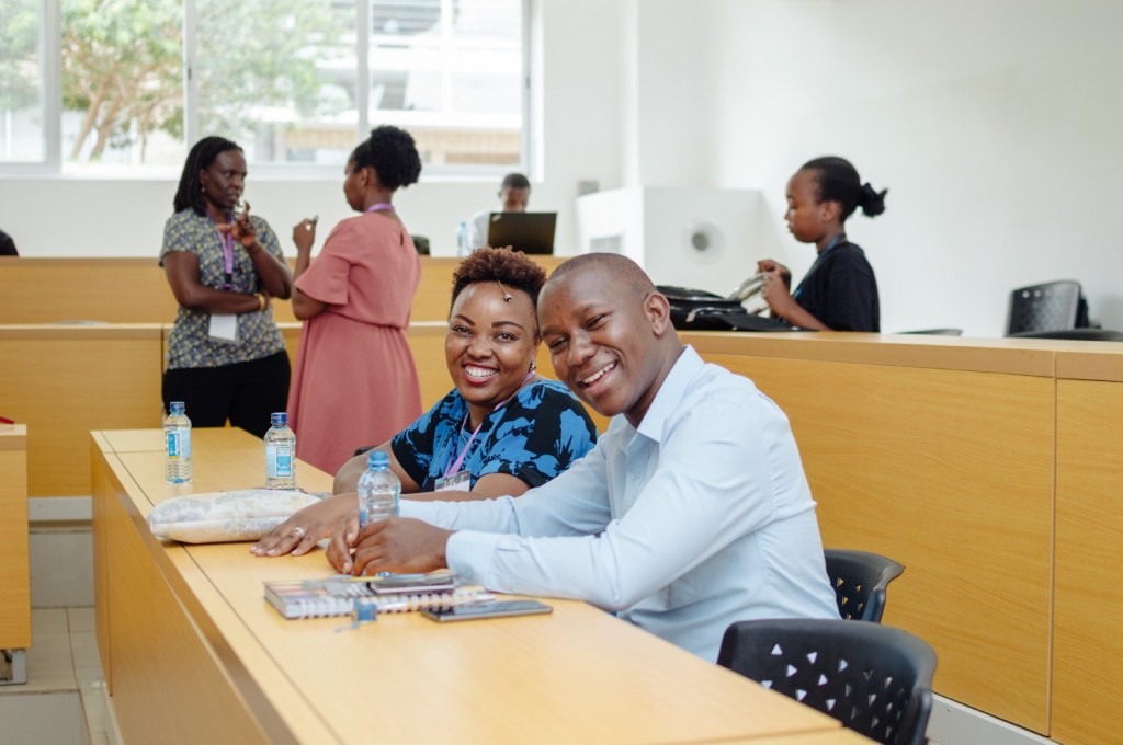 A pair of people sit together at a desk in a lecture hall.