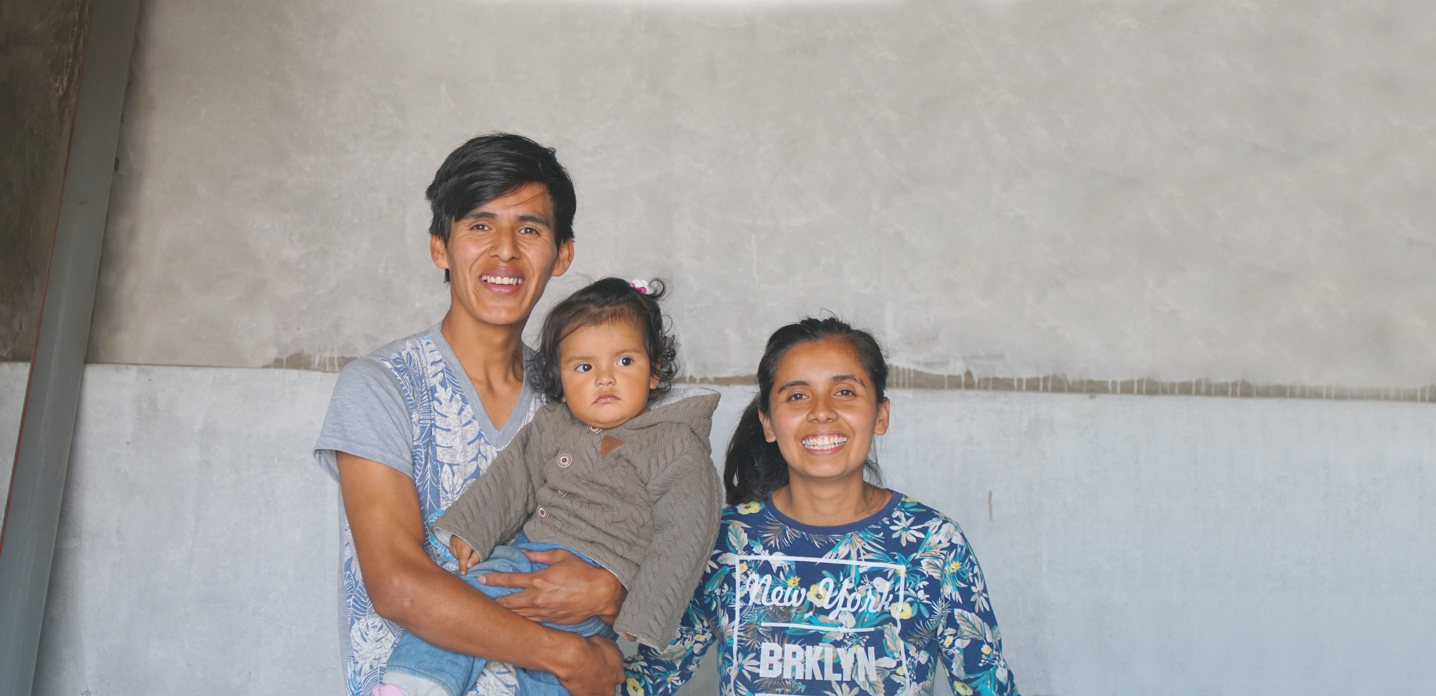 A mother and father stand together holding their baby.