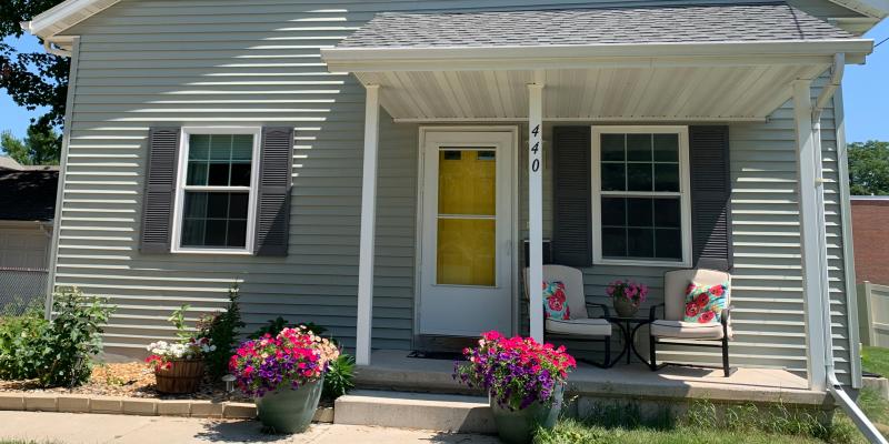 Habitat house with yellow door and pink flowers blooming in front.