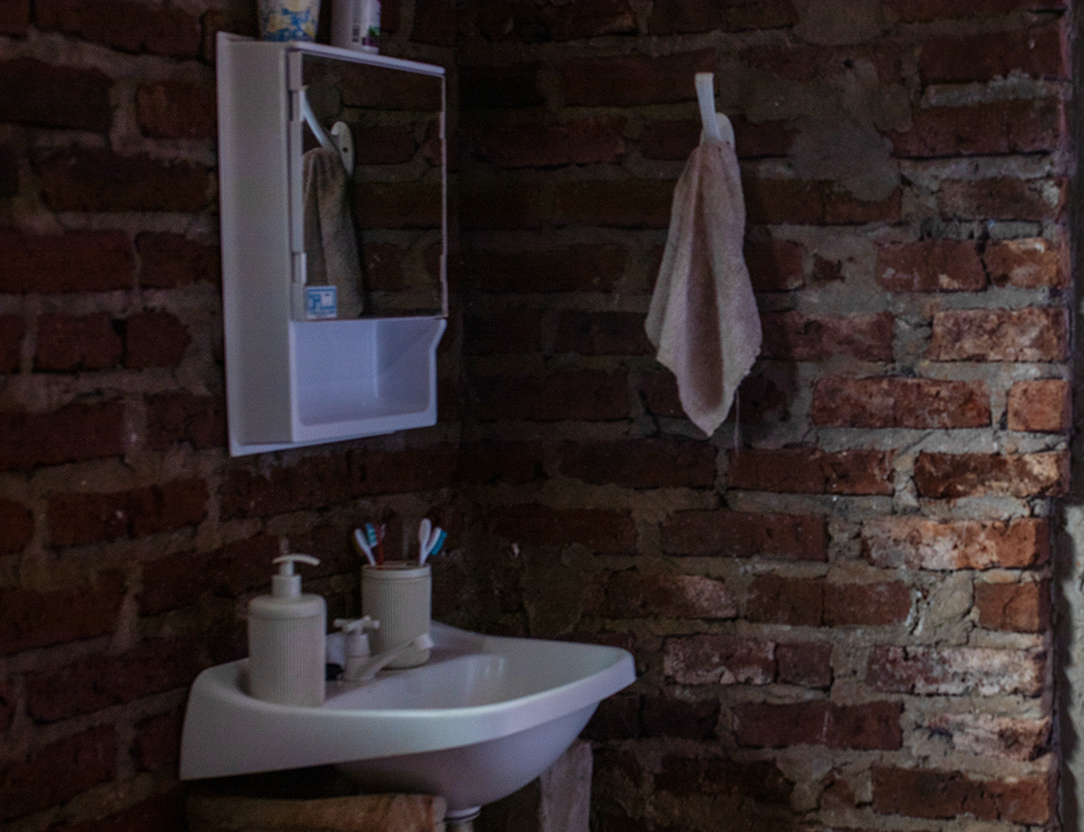 Corner of a home with brick walls, showing a sink and medicine cabinet with toiletries.