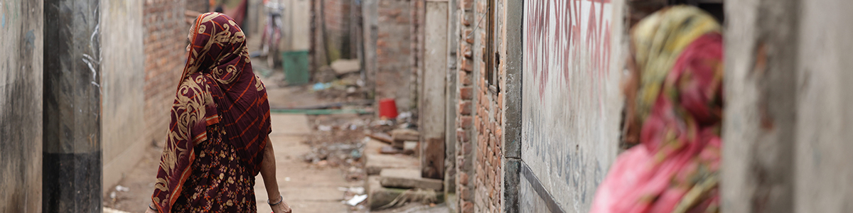 A woman walking down a dusty alleyway in an informal settlement.