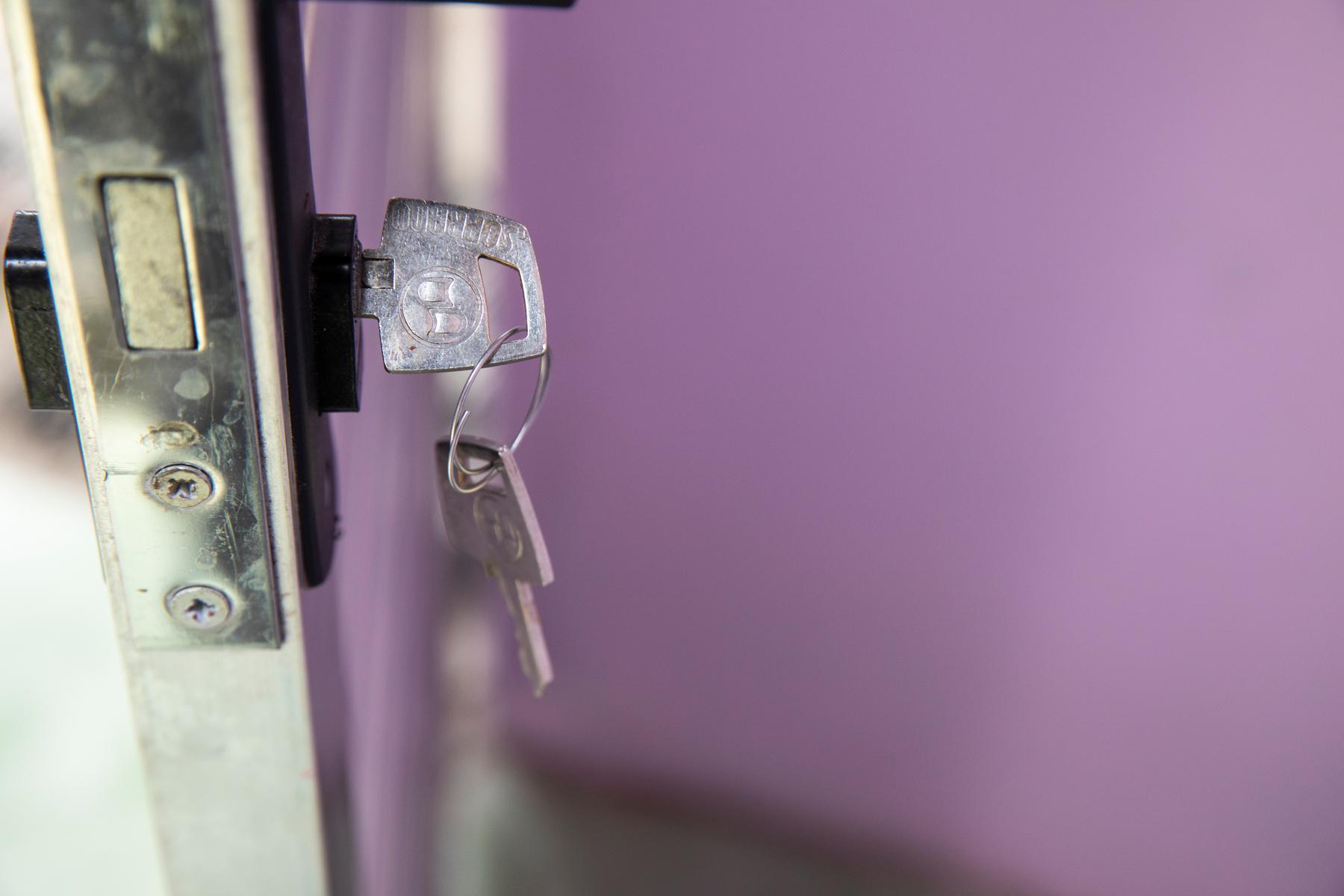 A door opening with a purple wall behind it showcasing a set of keys still in the lock.
