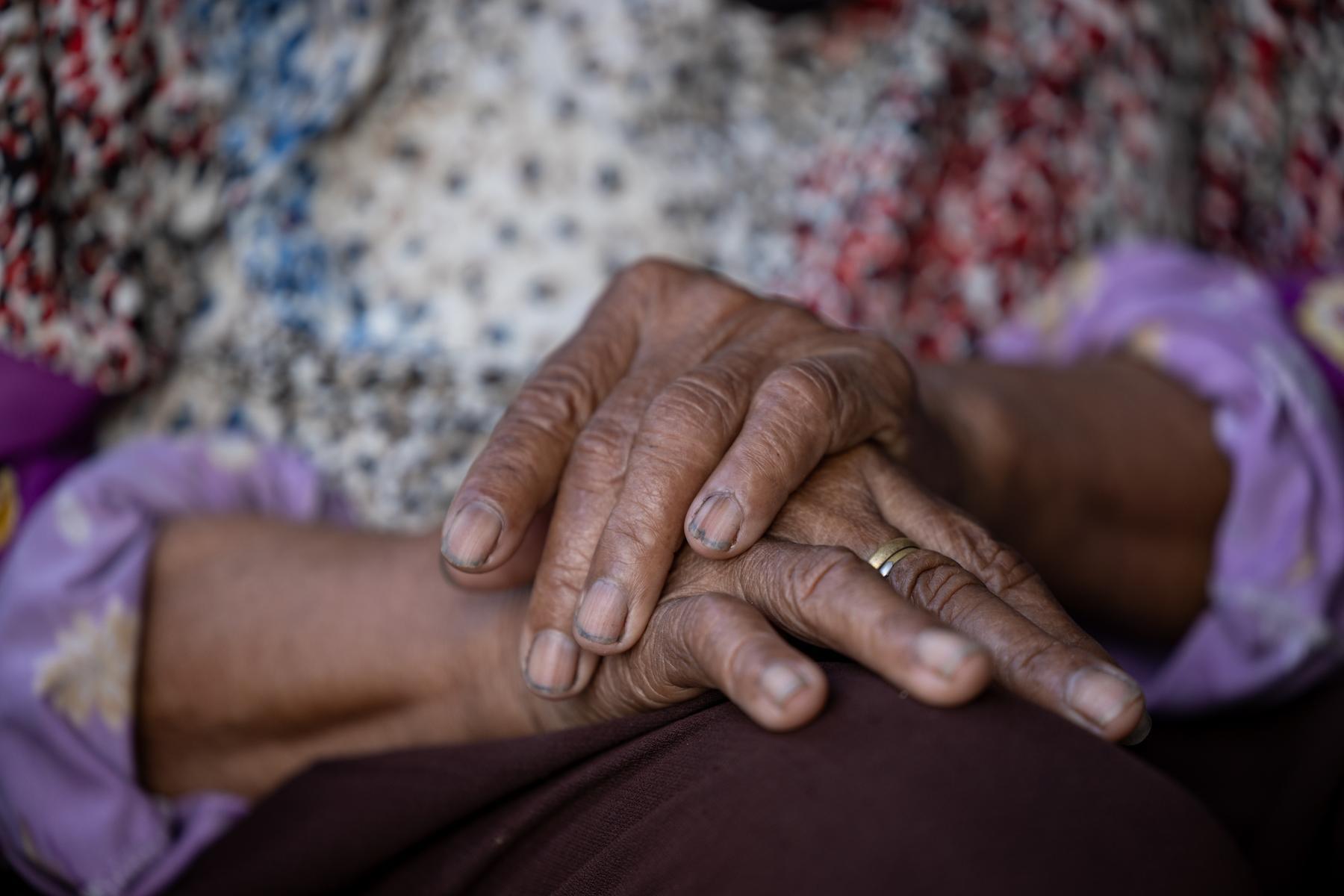 A pair of wrinkled hands clasped together on a lap.