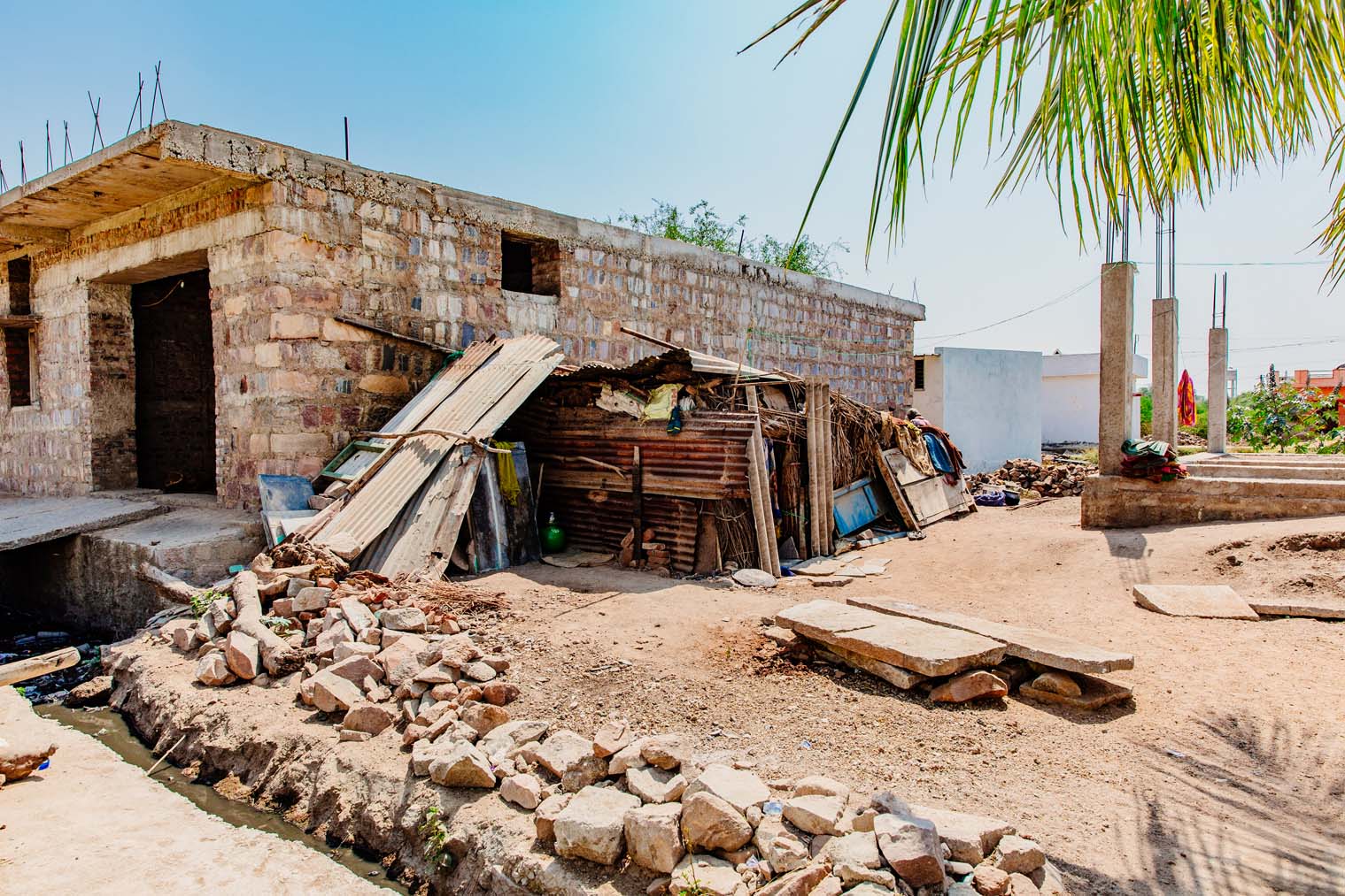 A brick house with open door and window frames in the midst of repair with a pile of lumber beside it.