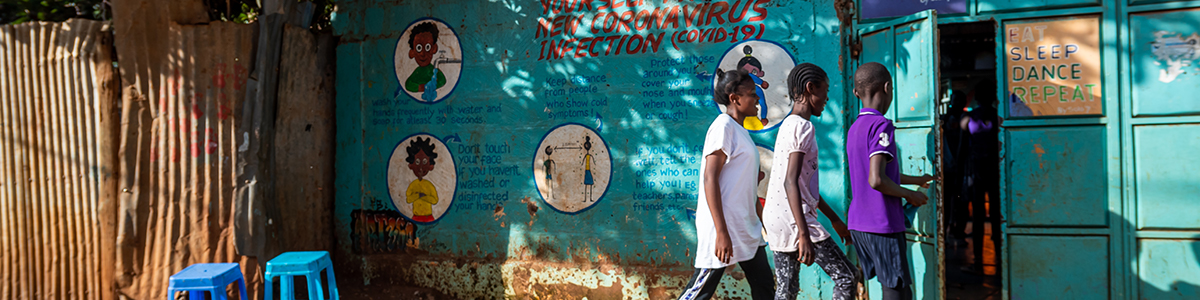 Three children walking into a blue shack in an informal settlement.