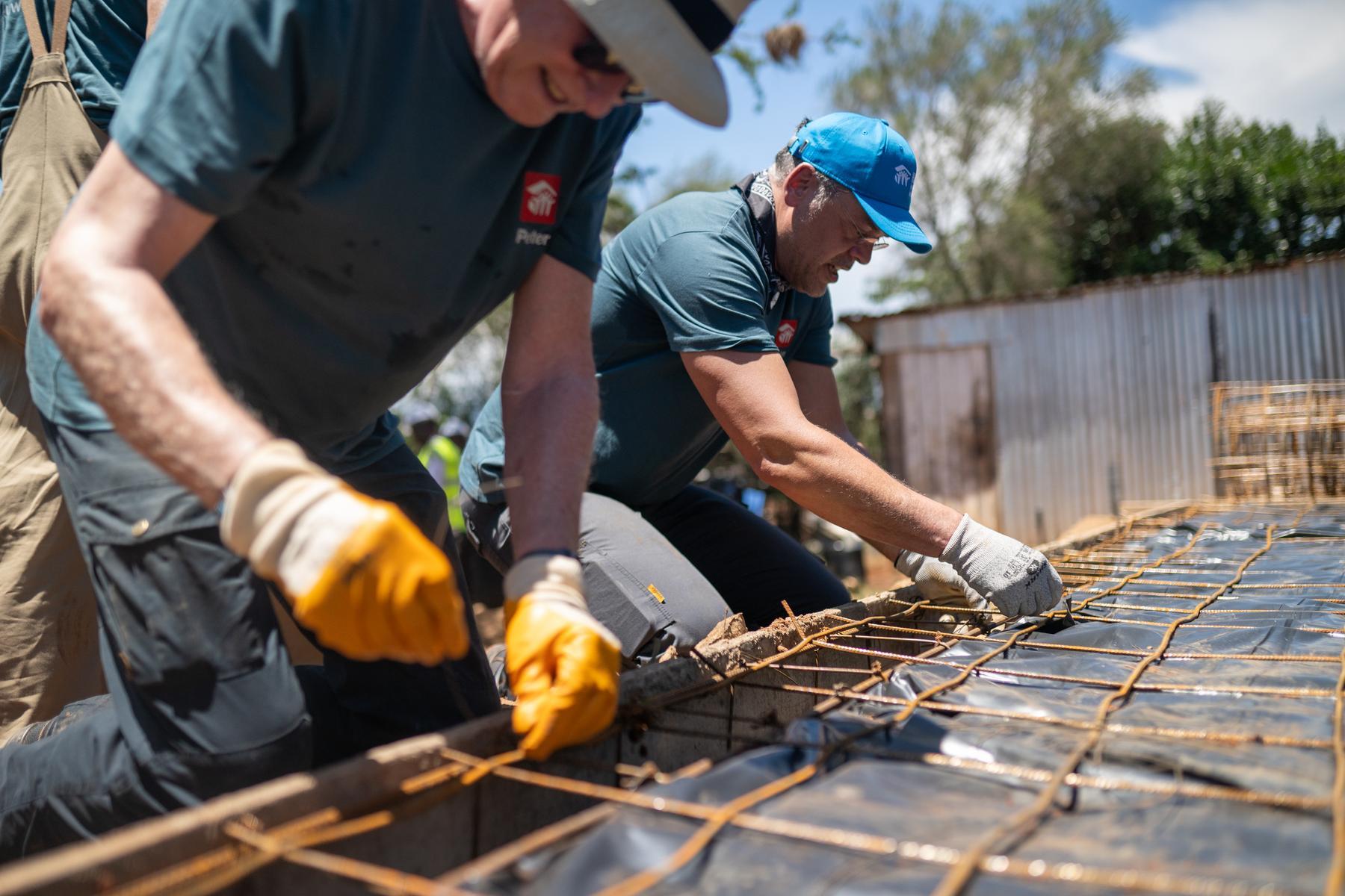 Two men in work gloves lean forward and work on a grid