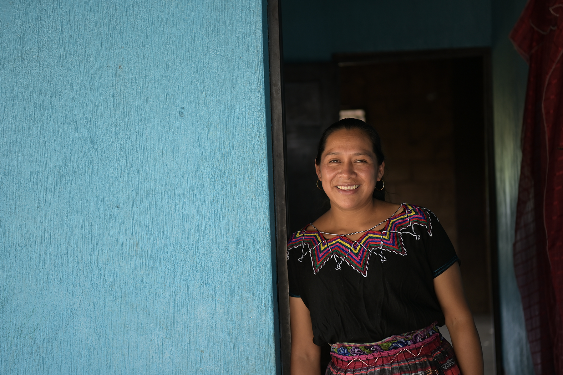 A woman smiles for the camera and leans against a blue wall. 