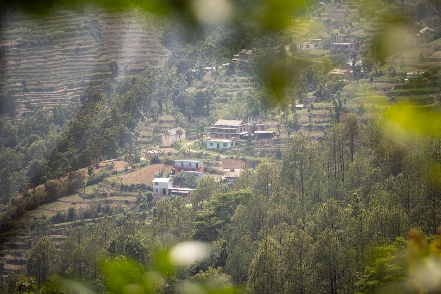 An image of hilltop community in Nepal from afar. There are leaves in the foreground framing the picture.