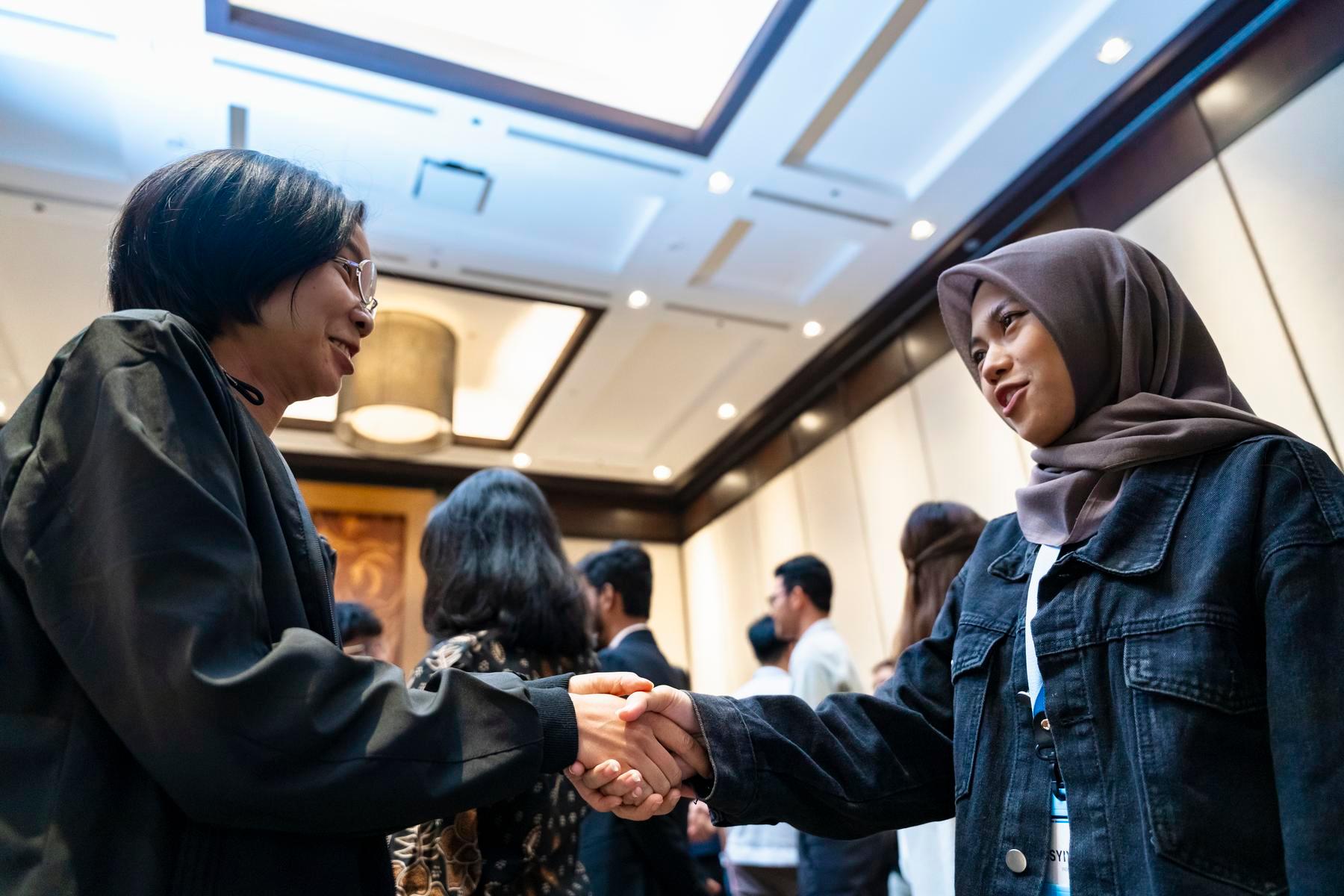 Two people shake hands and smile at each other.