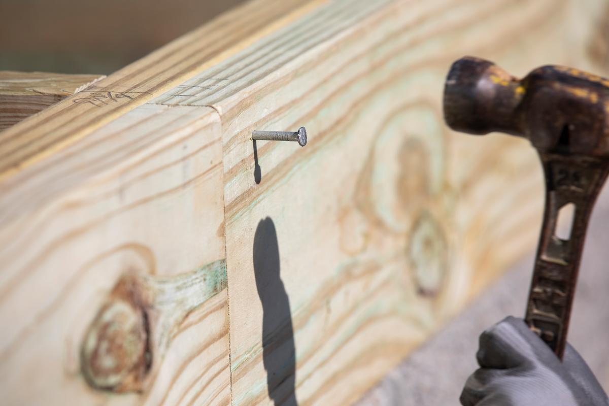 Close-up image of hammering nail into wood board.