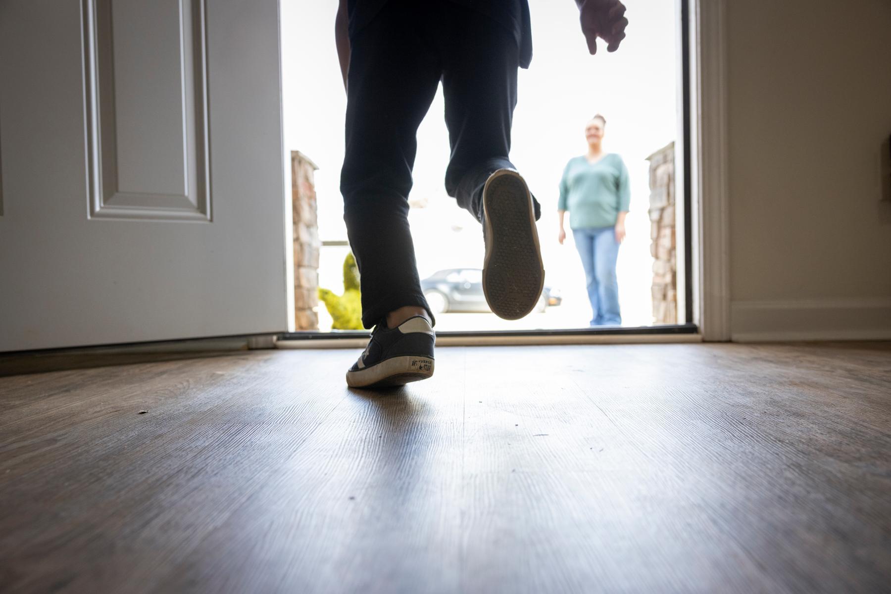 A child runs out the front door toward his mother who is waiting in the front yard.