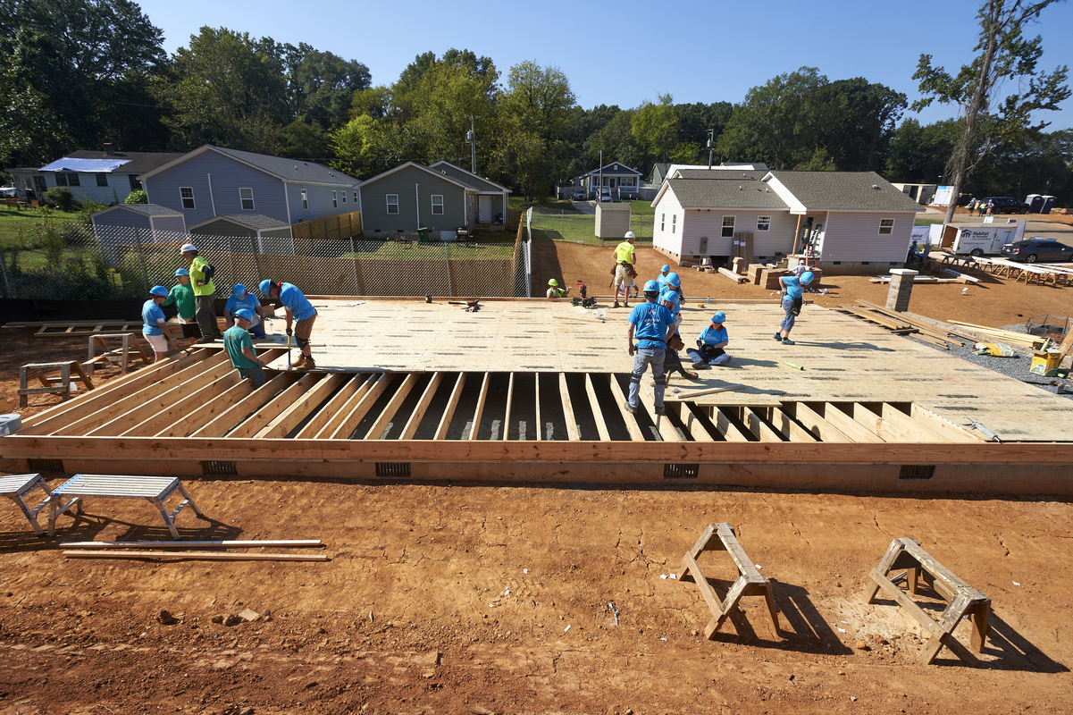 Wide view of construction site with volunteers hammering plywood over the boards of a platform.