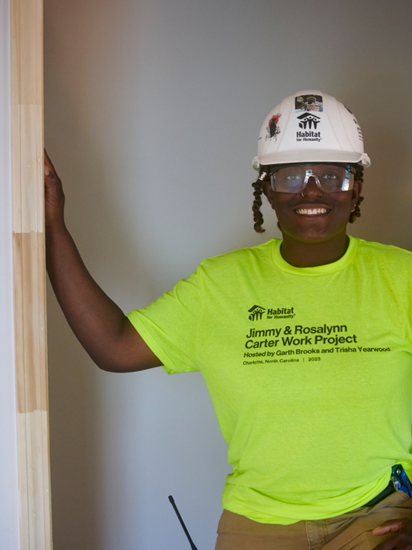 Amia stands with her arm in a doorway smiling at the camera.