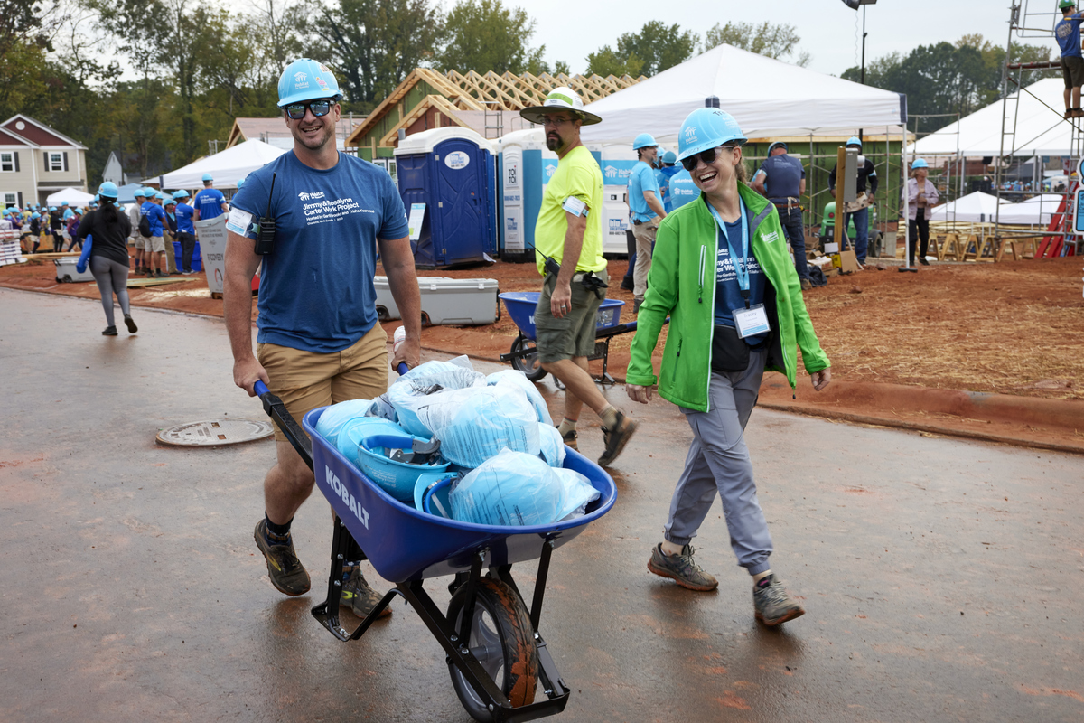 Volunteers walking through build site with wheelbarrow of hardhats