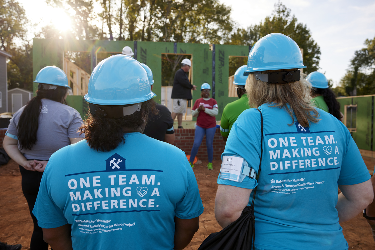 Volunteers listening to a homeowner speak in front of her future home