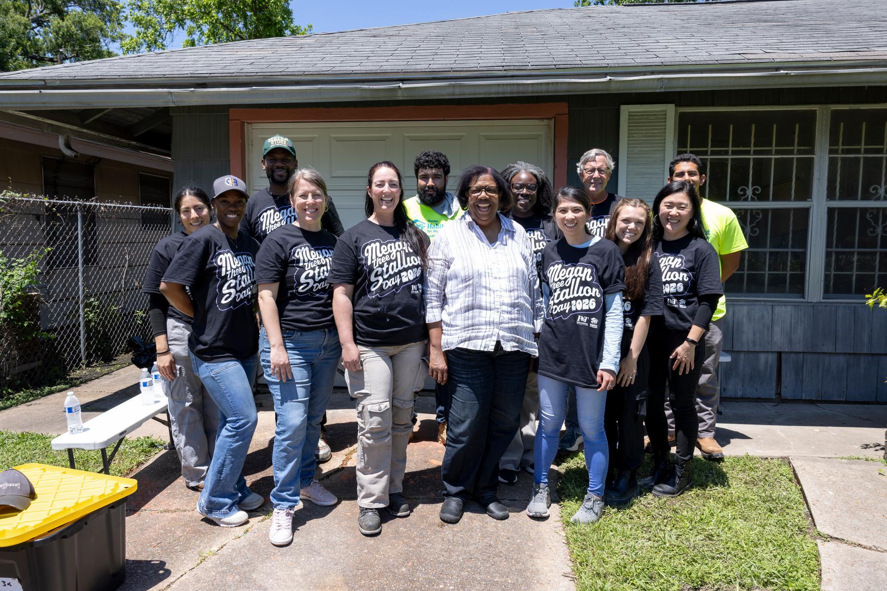 A group of Megan Thee Stallion volunteers stand outside a home with a homeowner.