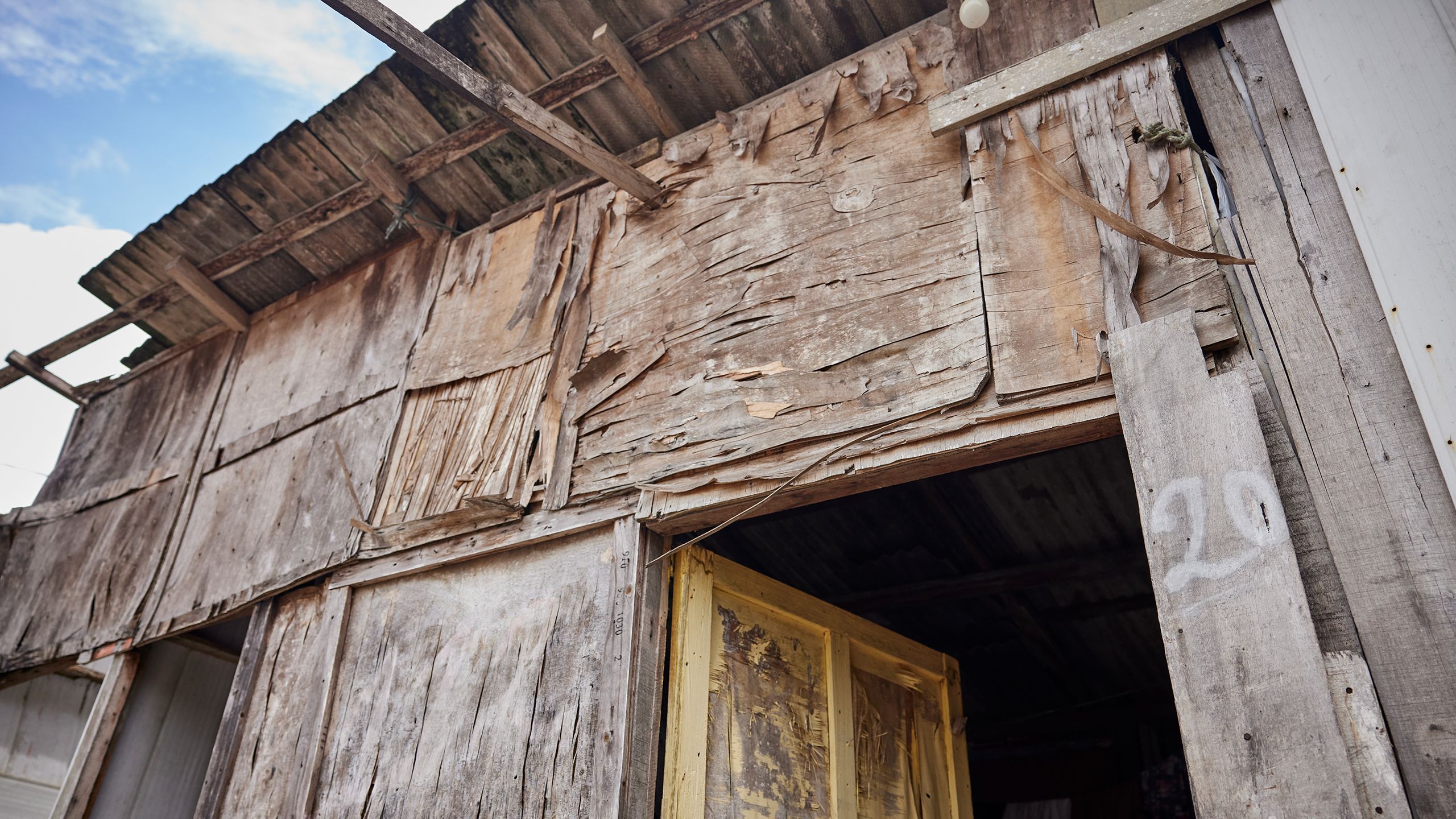 A house build of aging plywood sheets. The layers of plywood are peeling off and beginning to separate from the house's frame..