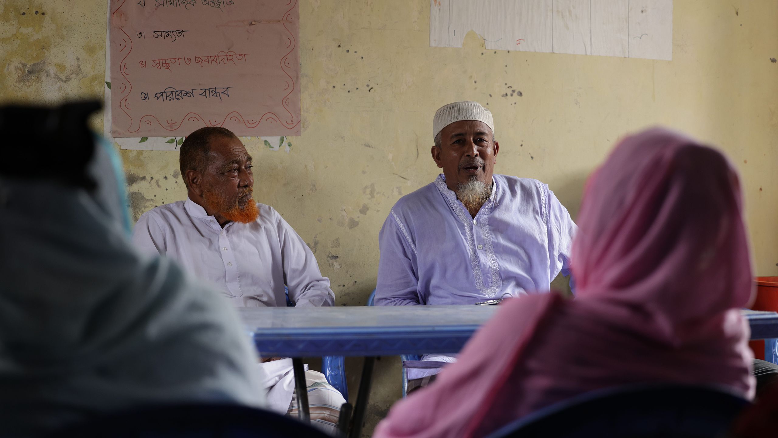 Raje and another community leader sit in a meeting room across the table from other Beguntila residents, deep in conversation.