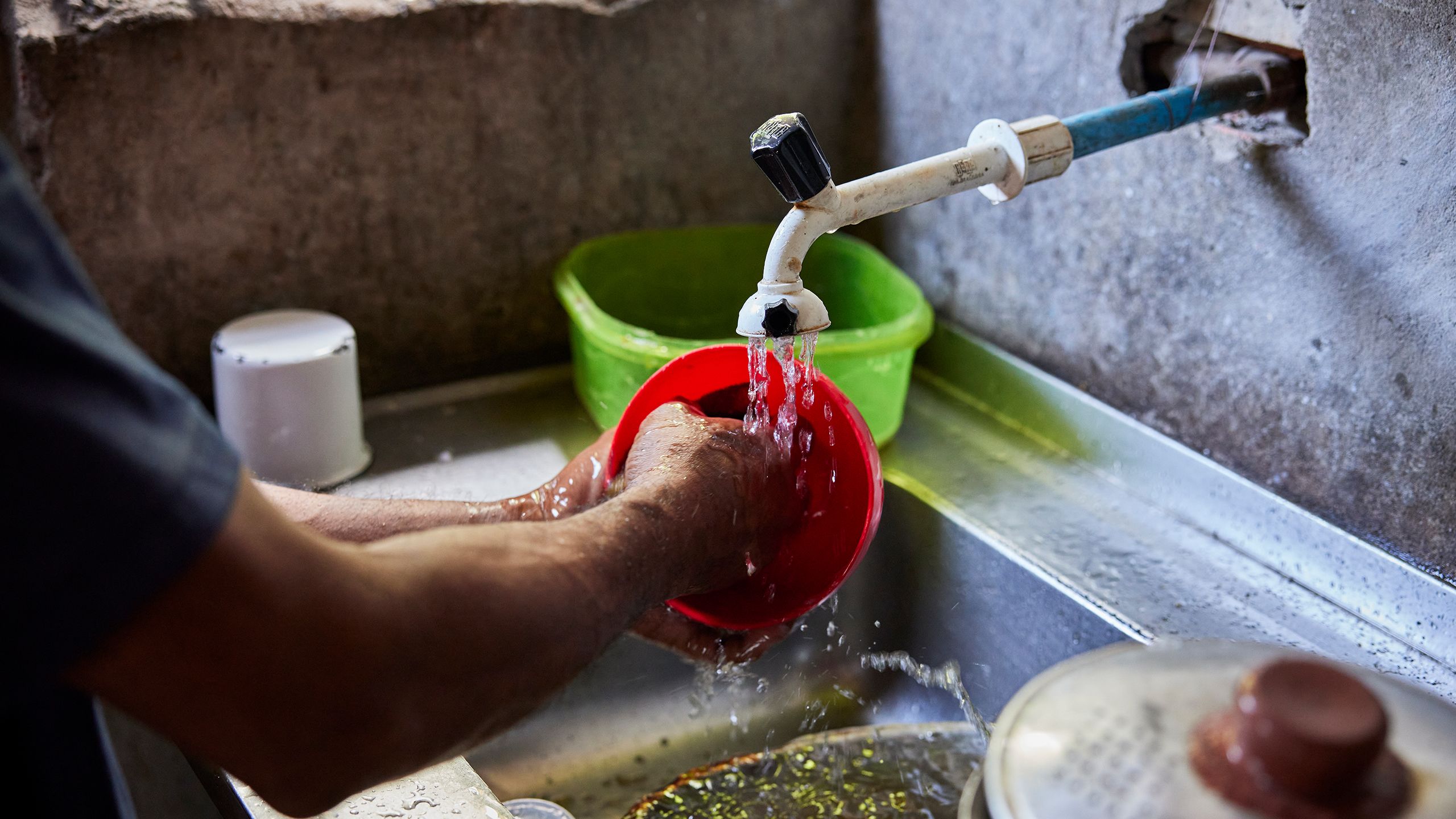 A woman washes a plastic bowl under a roughly installed faucet.