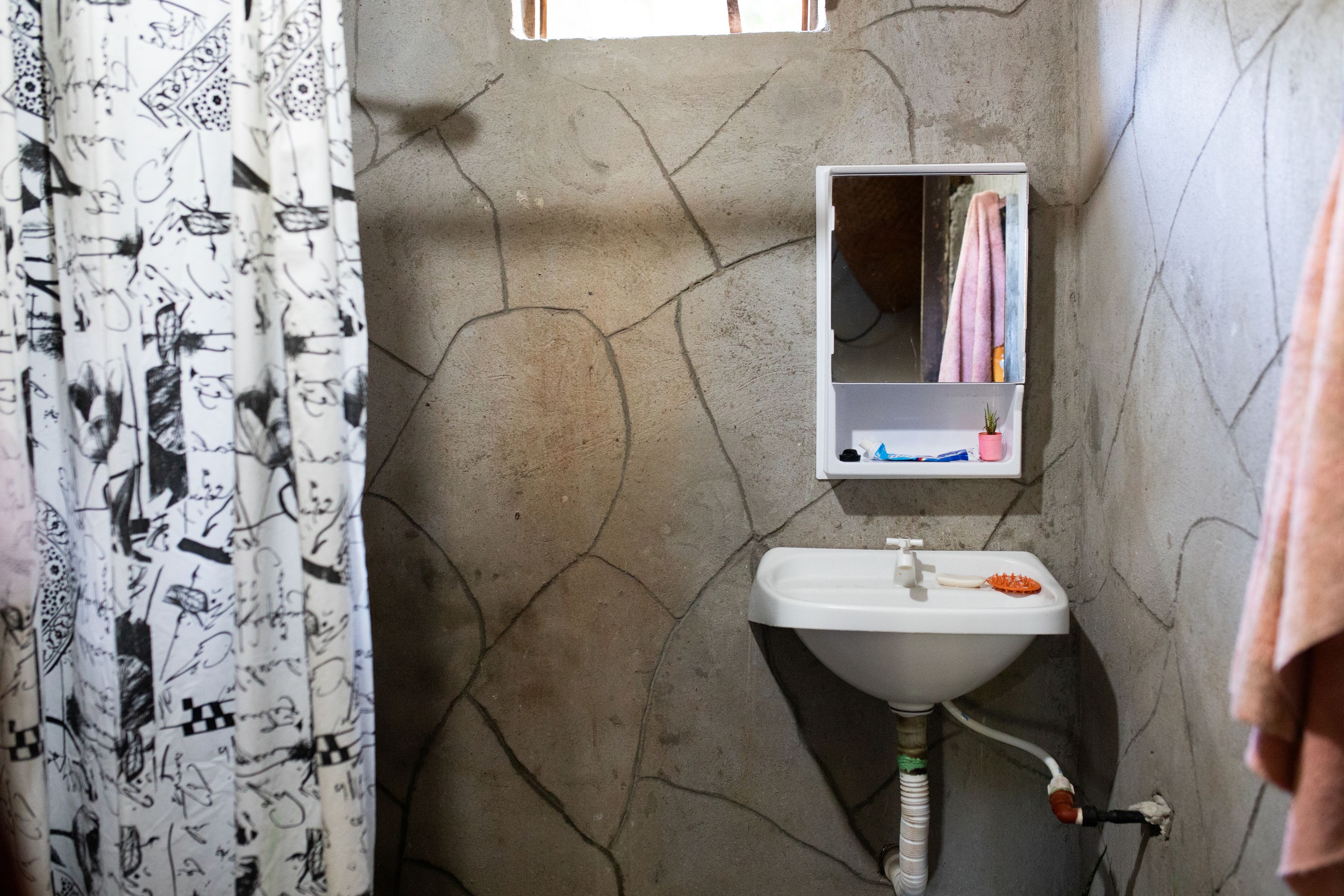 Alejandra's newly built bathroom with a black and white shower curtain, medicine cabinet, and sink with running water.