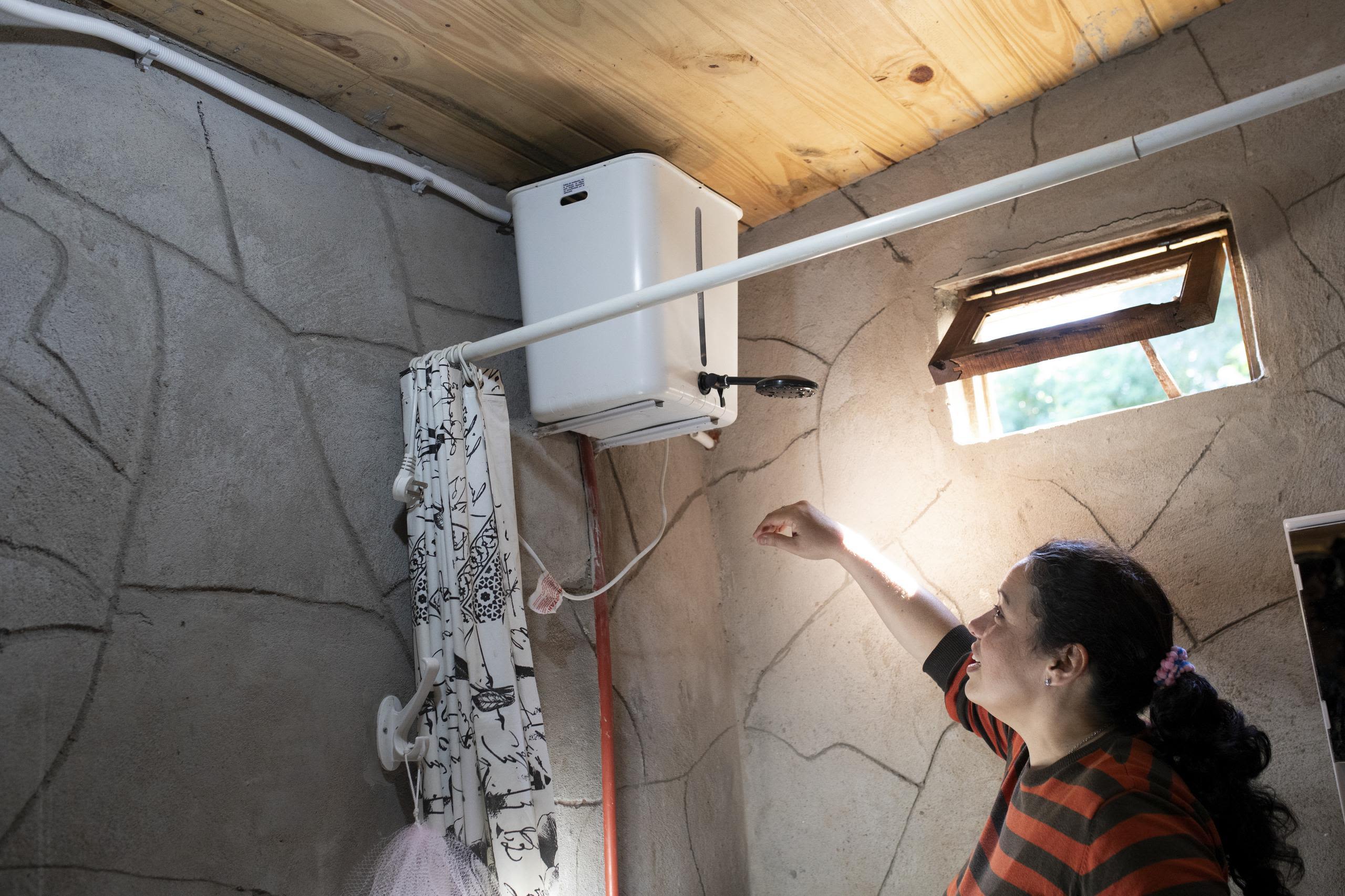 Alejandra standing in her newly built shower and bathroom with her arm raised toward the shower head.