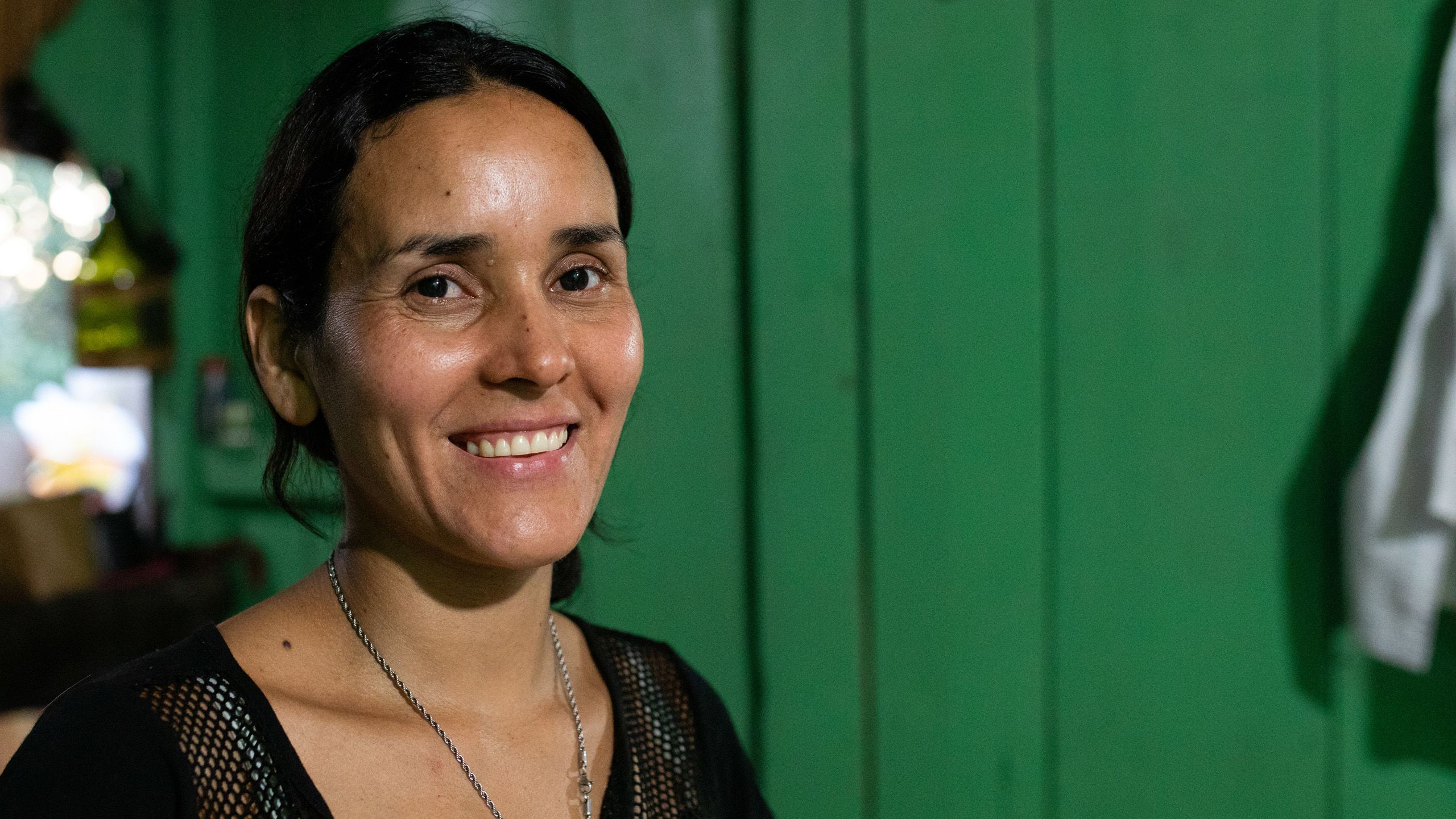 A close-up photo of Patricia looking directly at the camera and smiling in front of a green background.