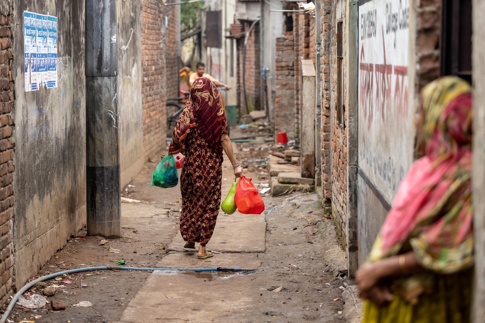 Woman carrying plastic bags of vegetables and groceries walking in Duaripara informal settlement, Dhaka, Bangladesh