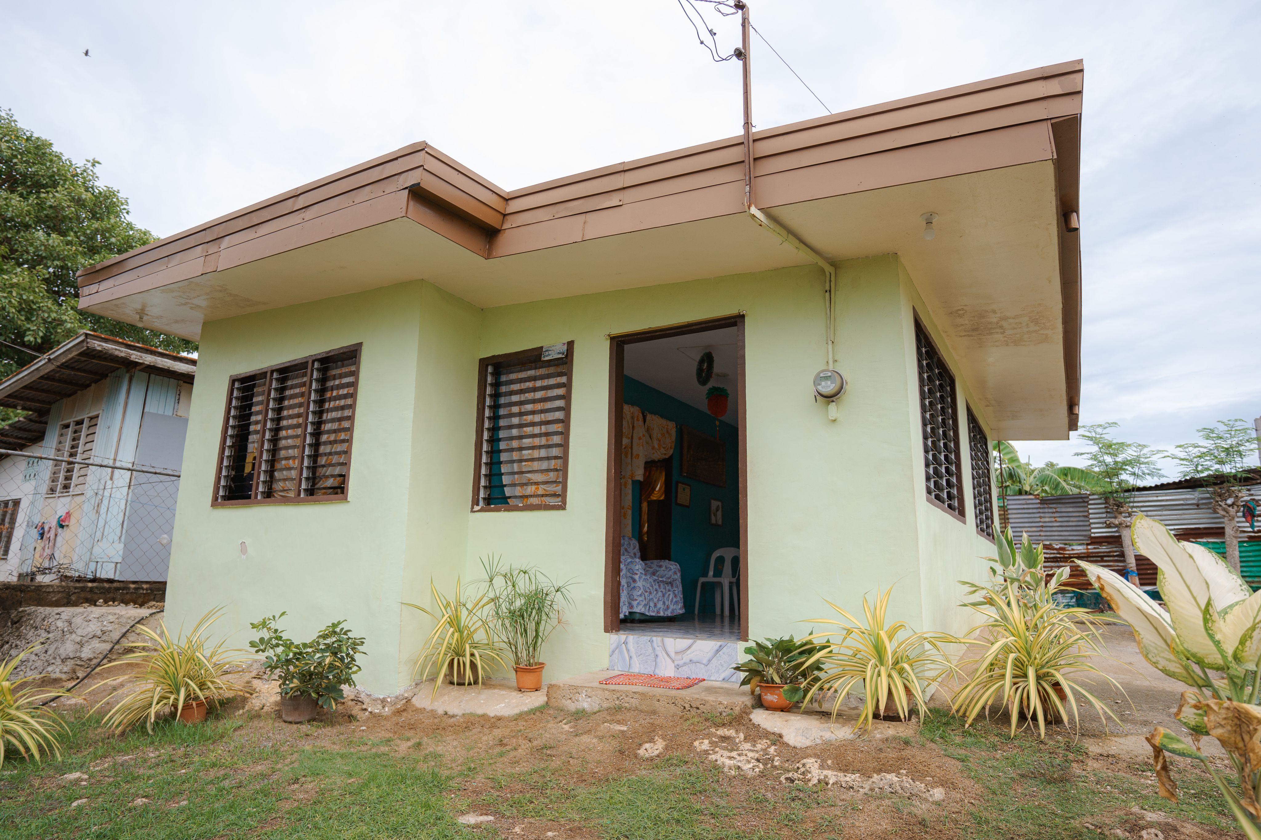 Exterior of a home in the Philippines, with a wide flat roof, louvered windows and pale green stucco walls.
