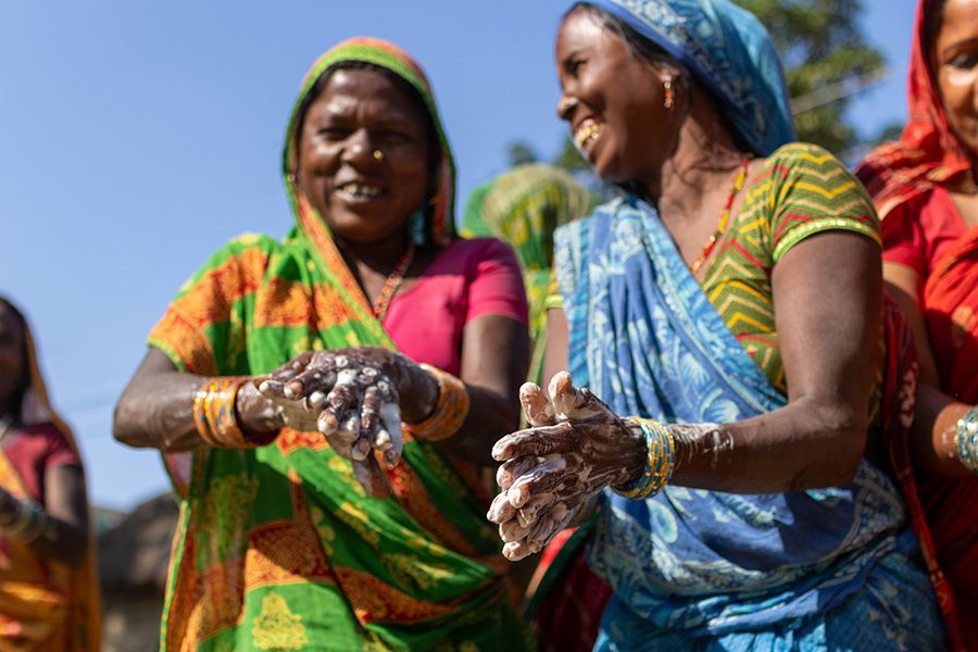 Photo of women washing their hands together. They are smiling and wearing colorful saris. 