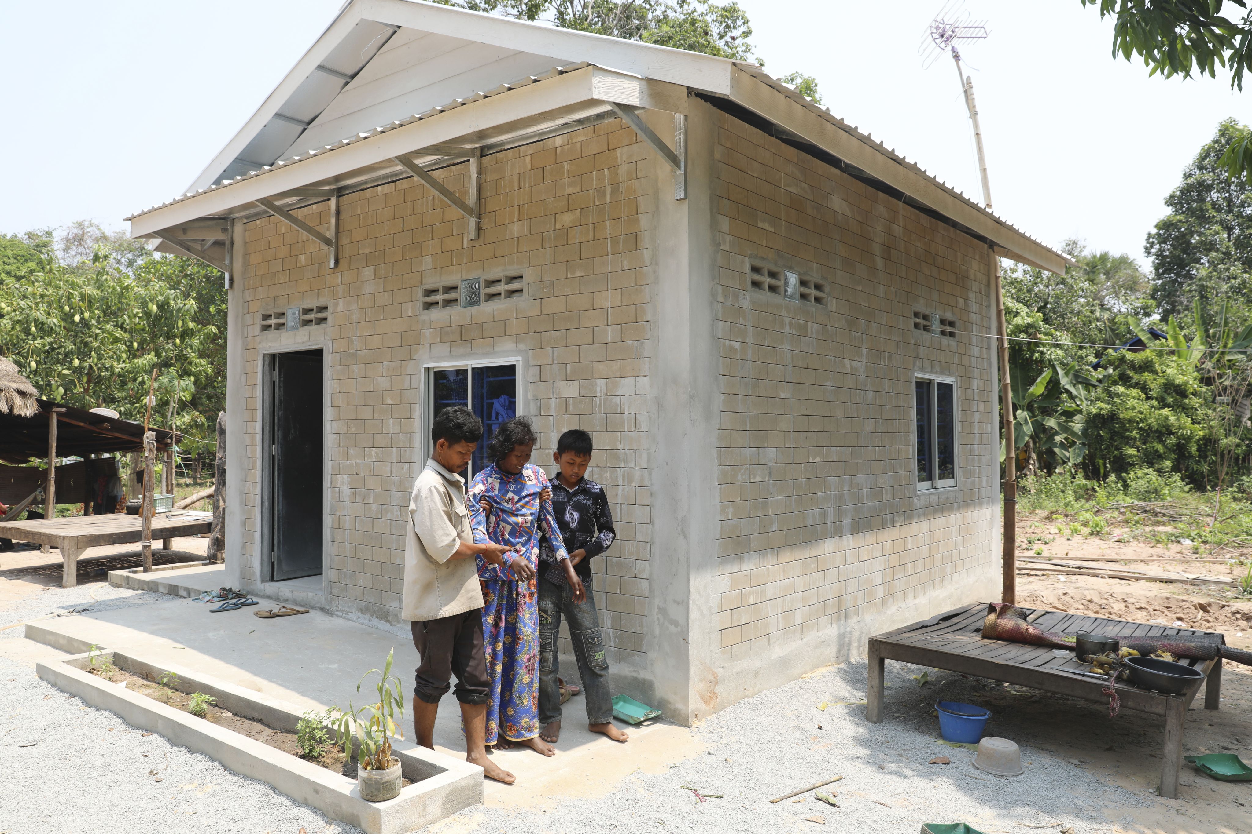 A man and boy help a woman walk down the ramp in front of their home.
