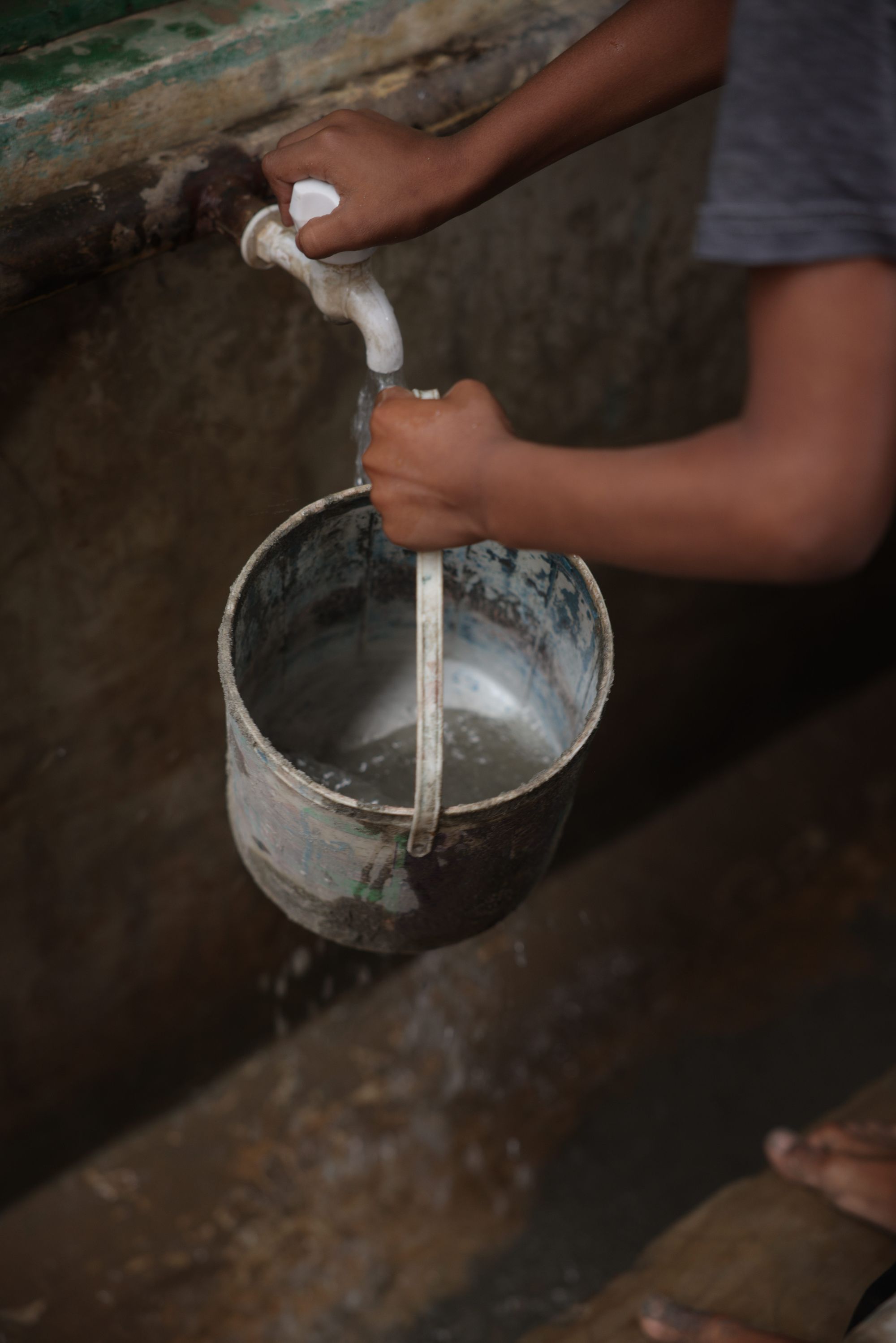 Closeup photo of hands filling a bucket with water from a spigot.