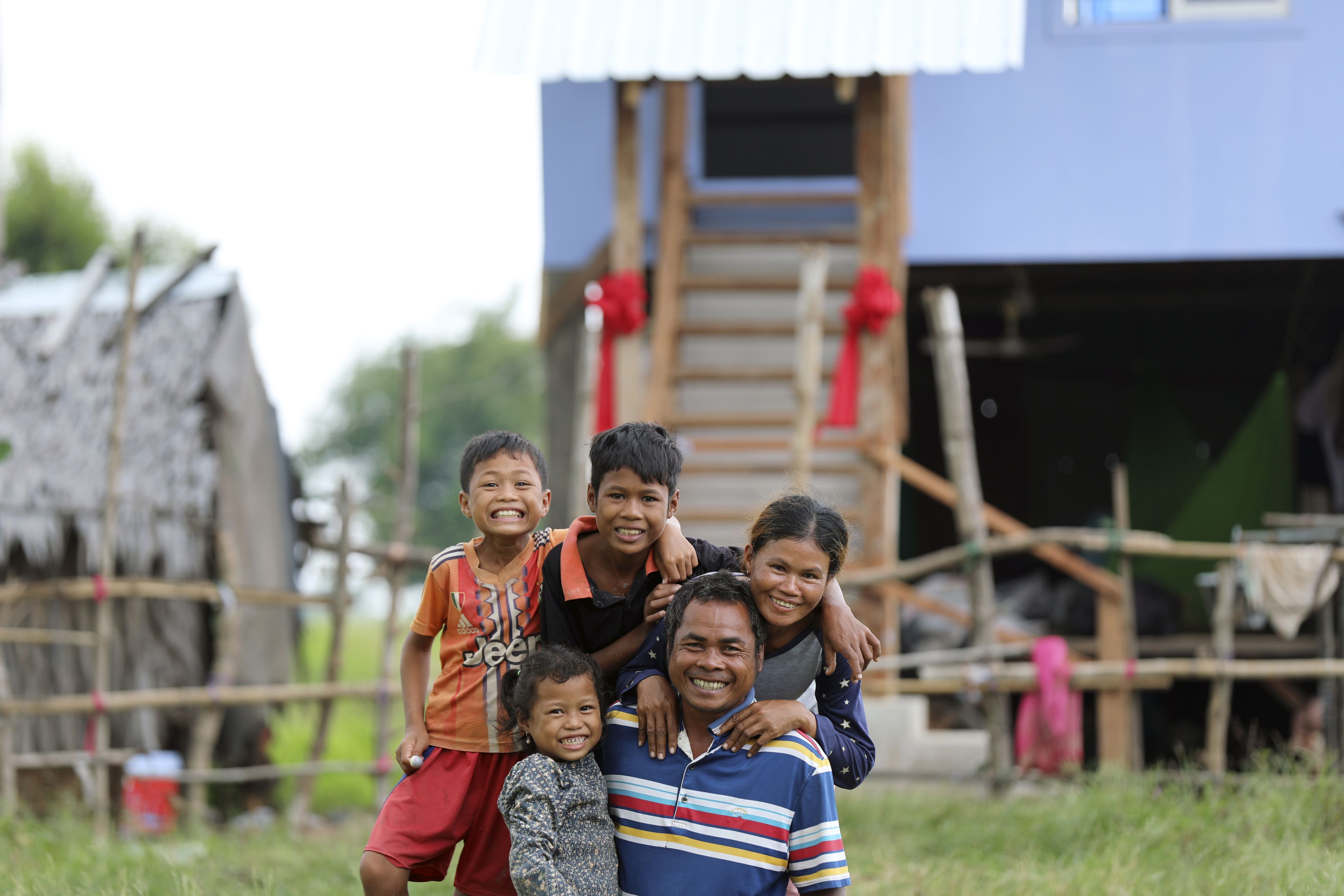 Smiling family of five hugs each other while posing in front of their elevated house.