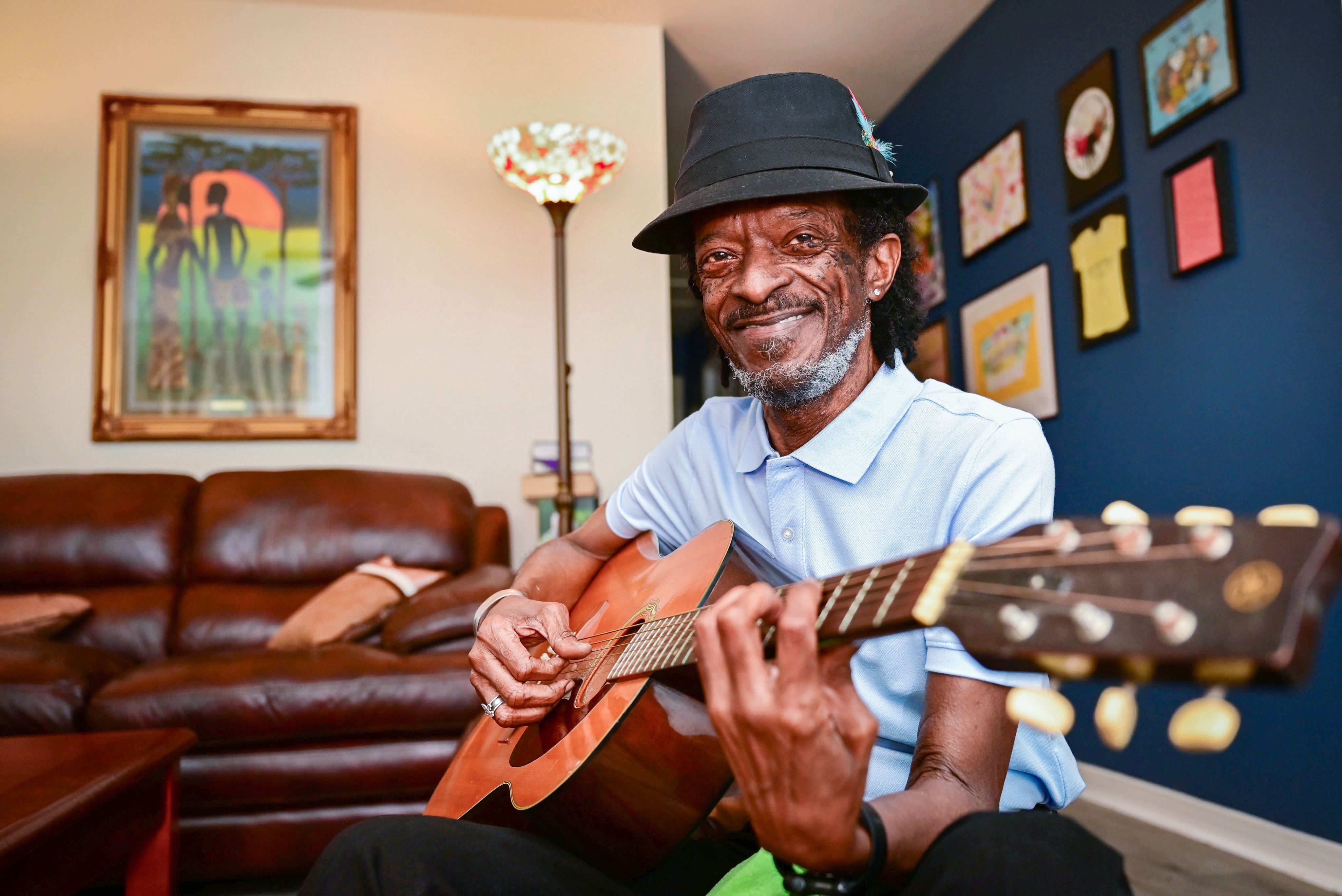 Habitat homeowner Michael Harris, smiling, sits in his new home playing guitar.