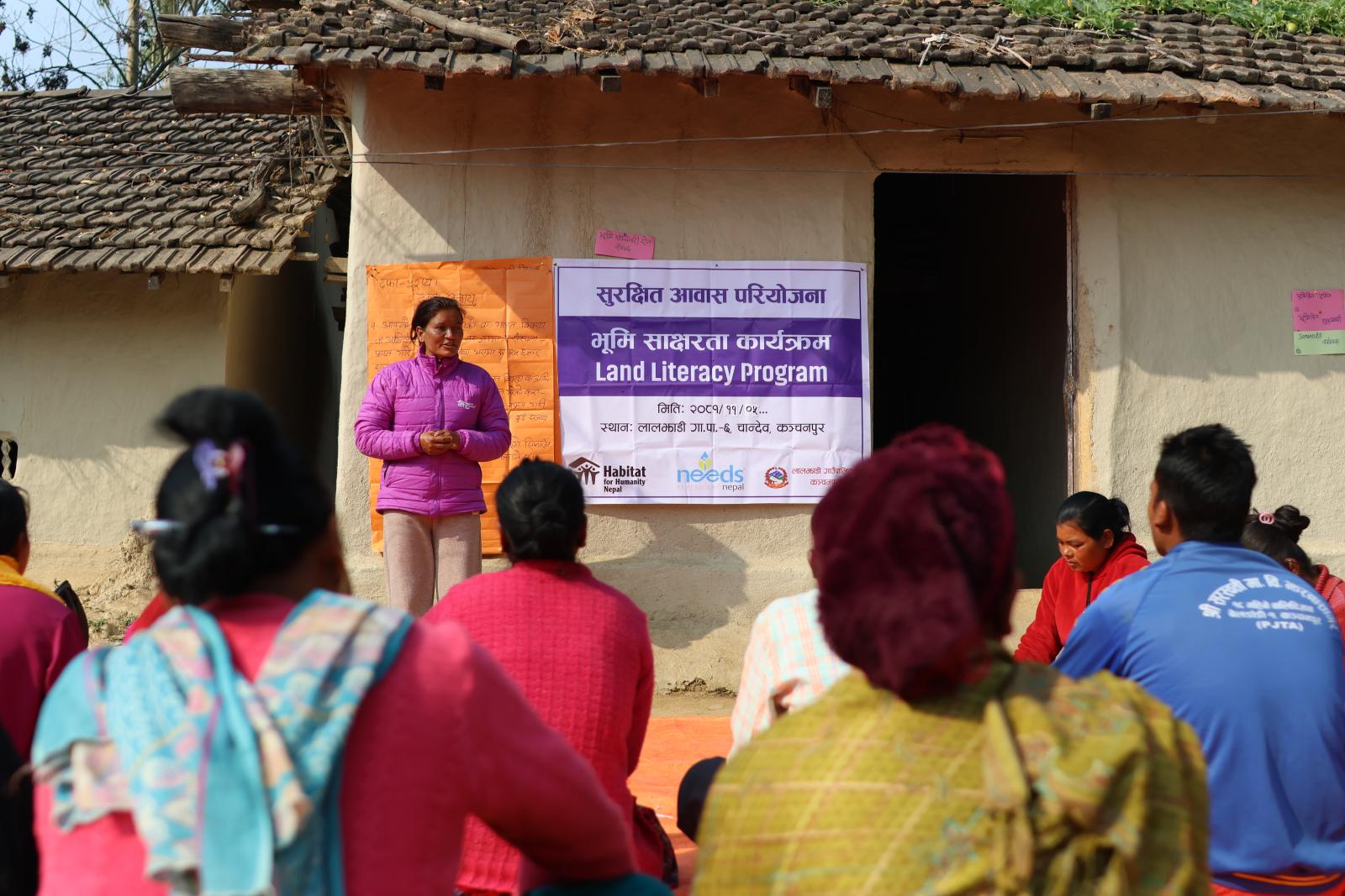 Person standing in front of a house, speaking to a group of people in the community.