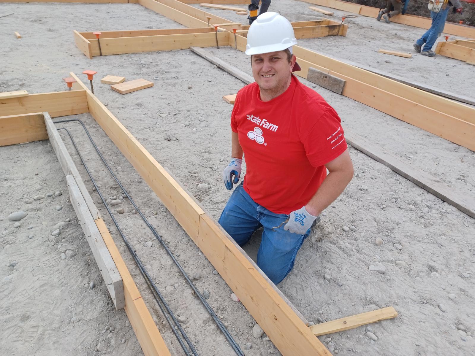 Man in red shirt and white hard hat posing next to part wood.