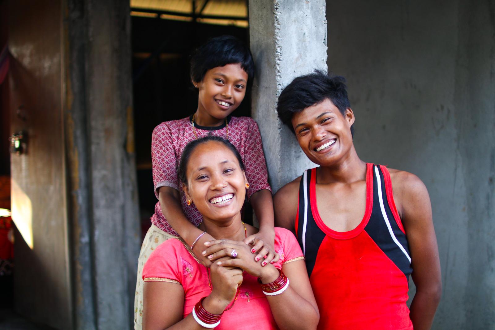 Smiling family of three sitting in front of their gray house.