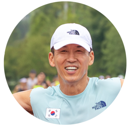 SeanKim is running and has his arms spread wide as he looks victorious. He is wearing a green sleeveless shirt and a white ballcap.